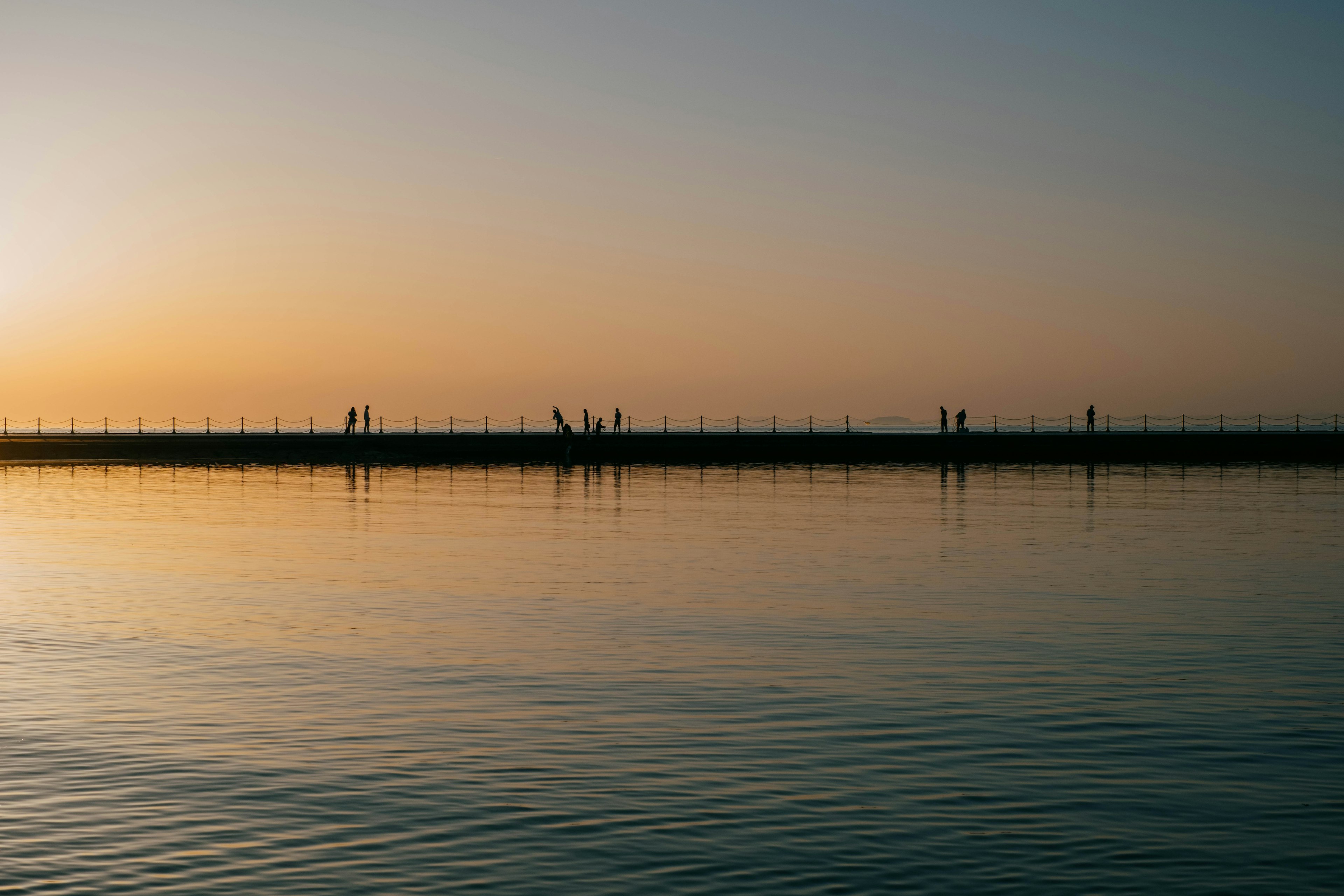 Figure in ombra su un molo al tramonto riflettendo sull'acqua calma