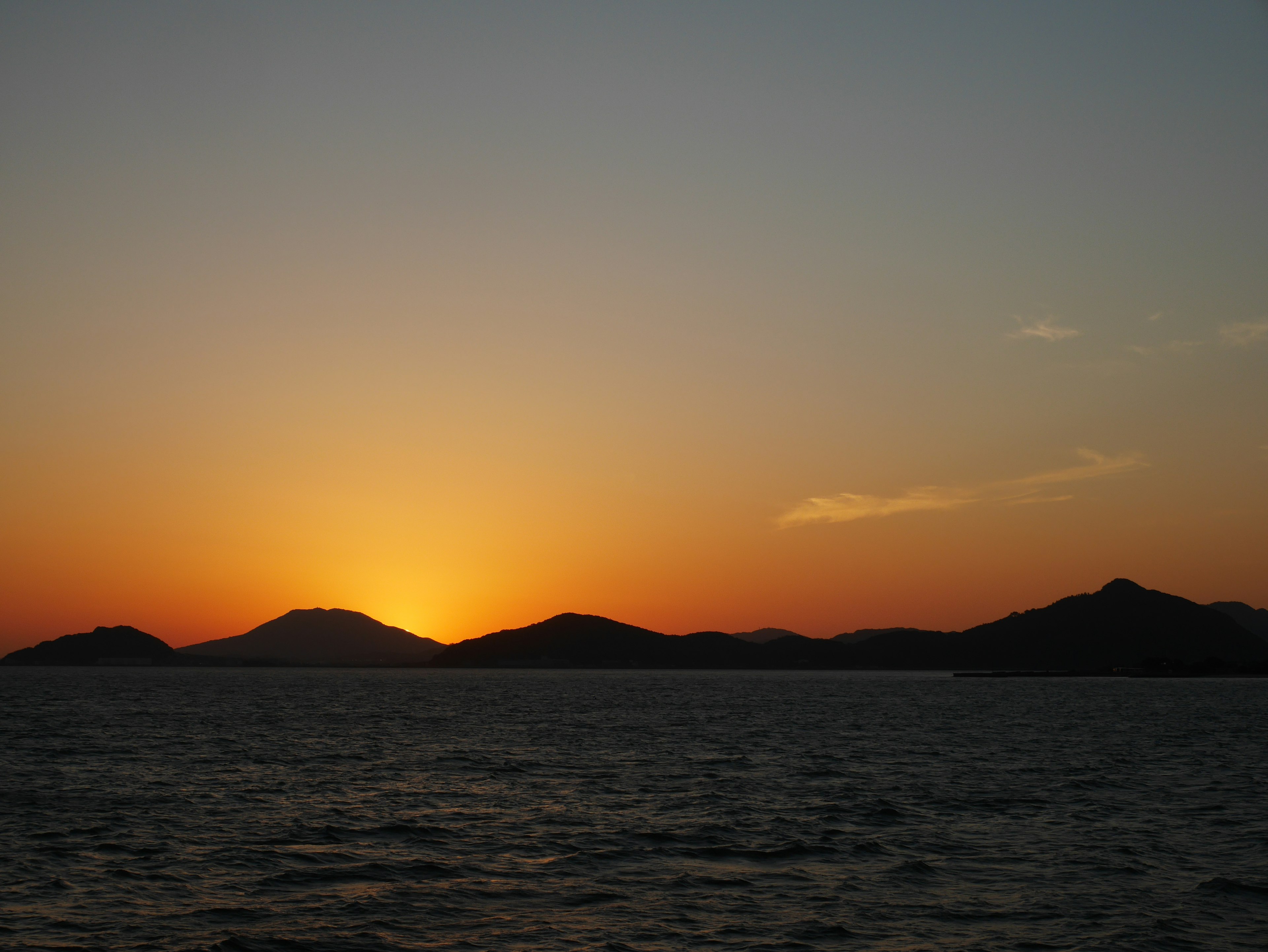 Sonnenuntergang über dem Meer mit Silhouetten von Bergen