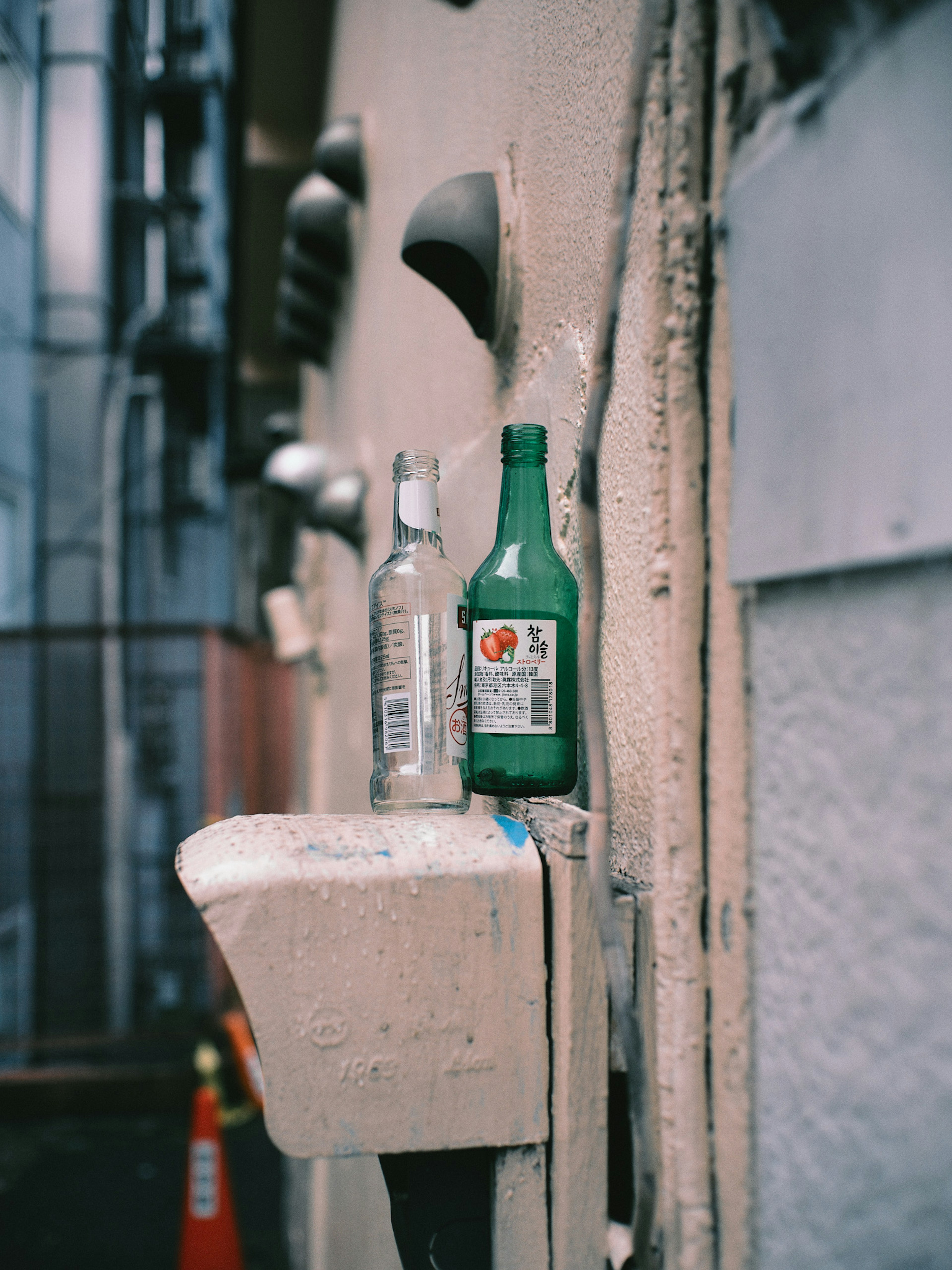 Scene featuring a clear bottle and a green bottle placed against a wall