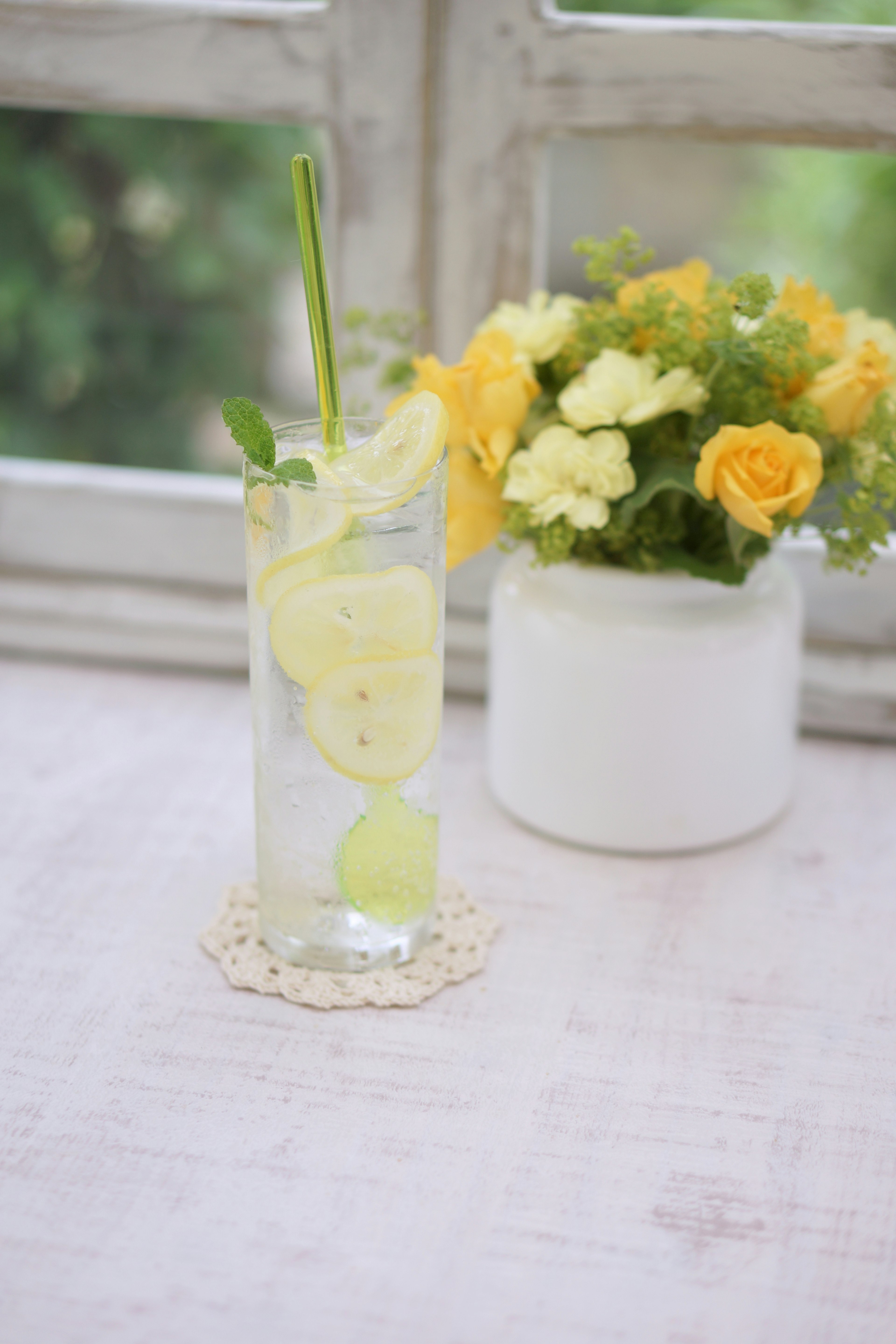 Bebida refrescante de limón con menta al lado de un jarrón de flores amarillas