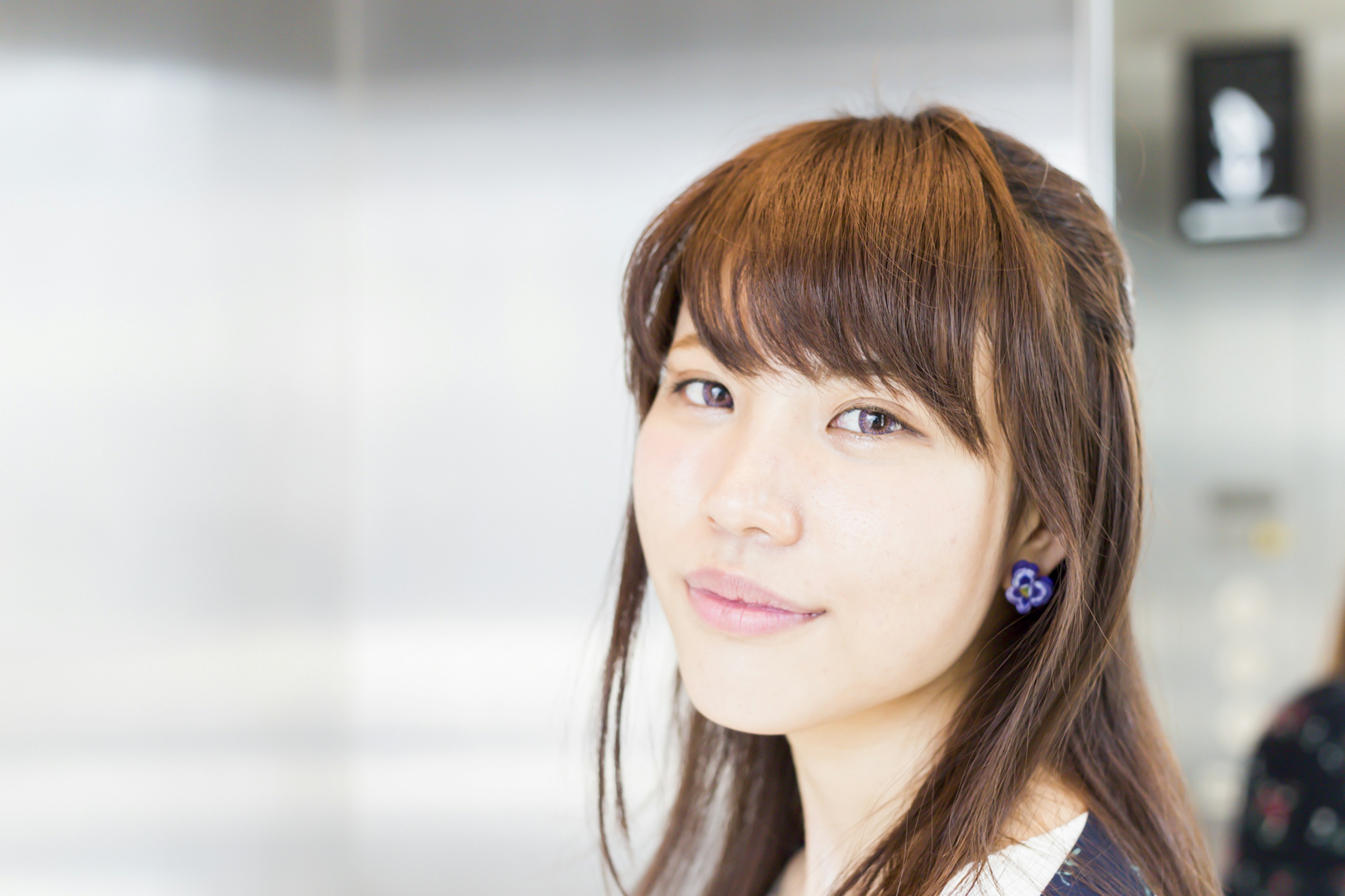 Portrait of a young woman with long brown hair wearing blue earrings blurred metallic background