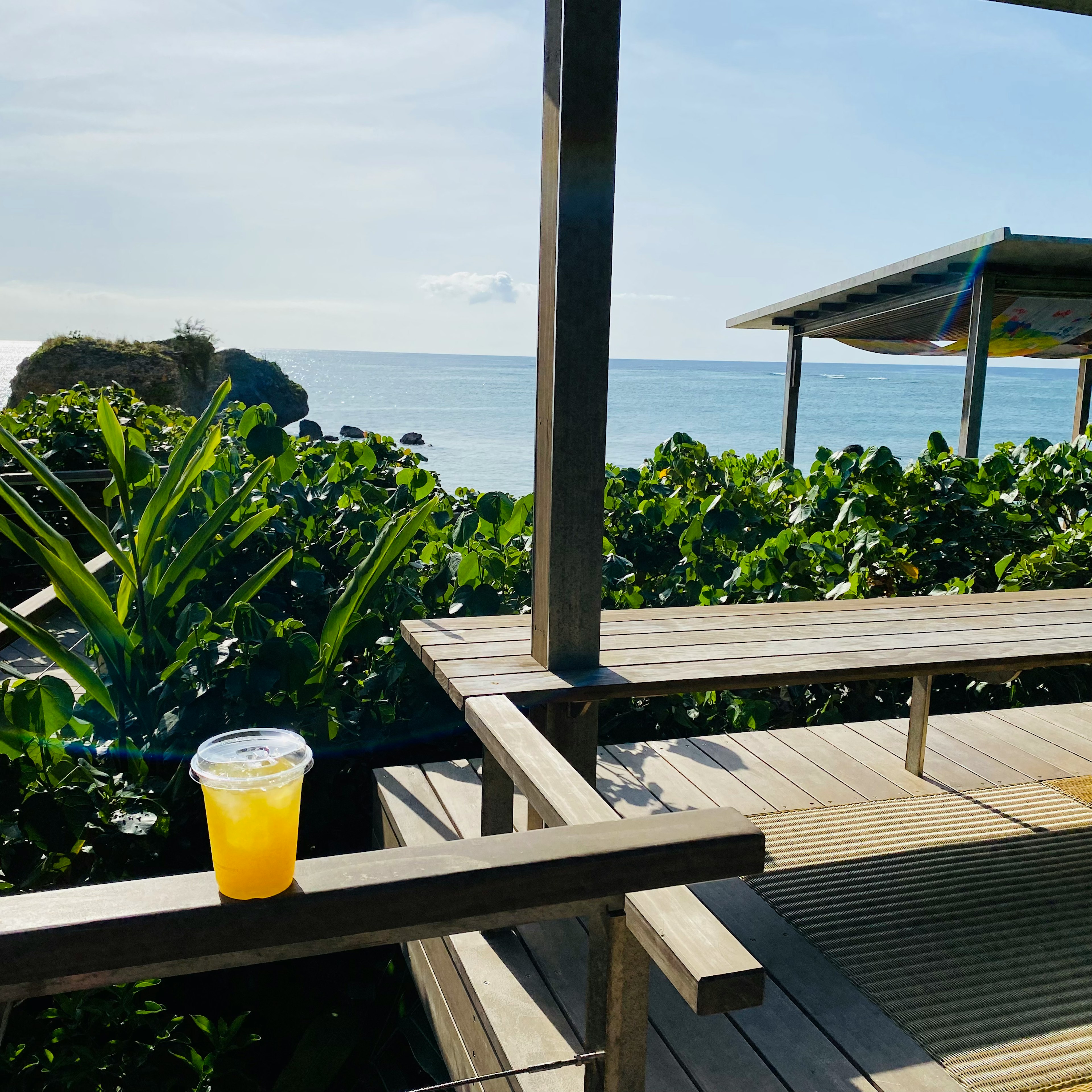 海を背景にしたカフェのテラスに置かれたオレンジジュースのカップ