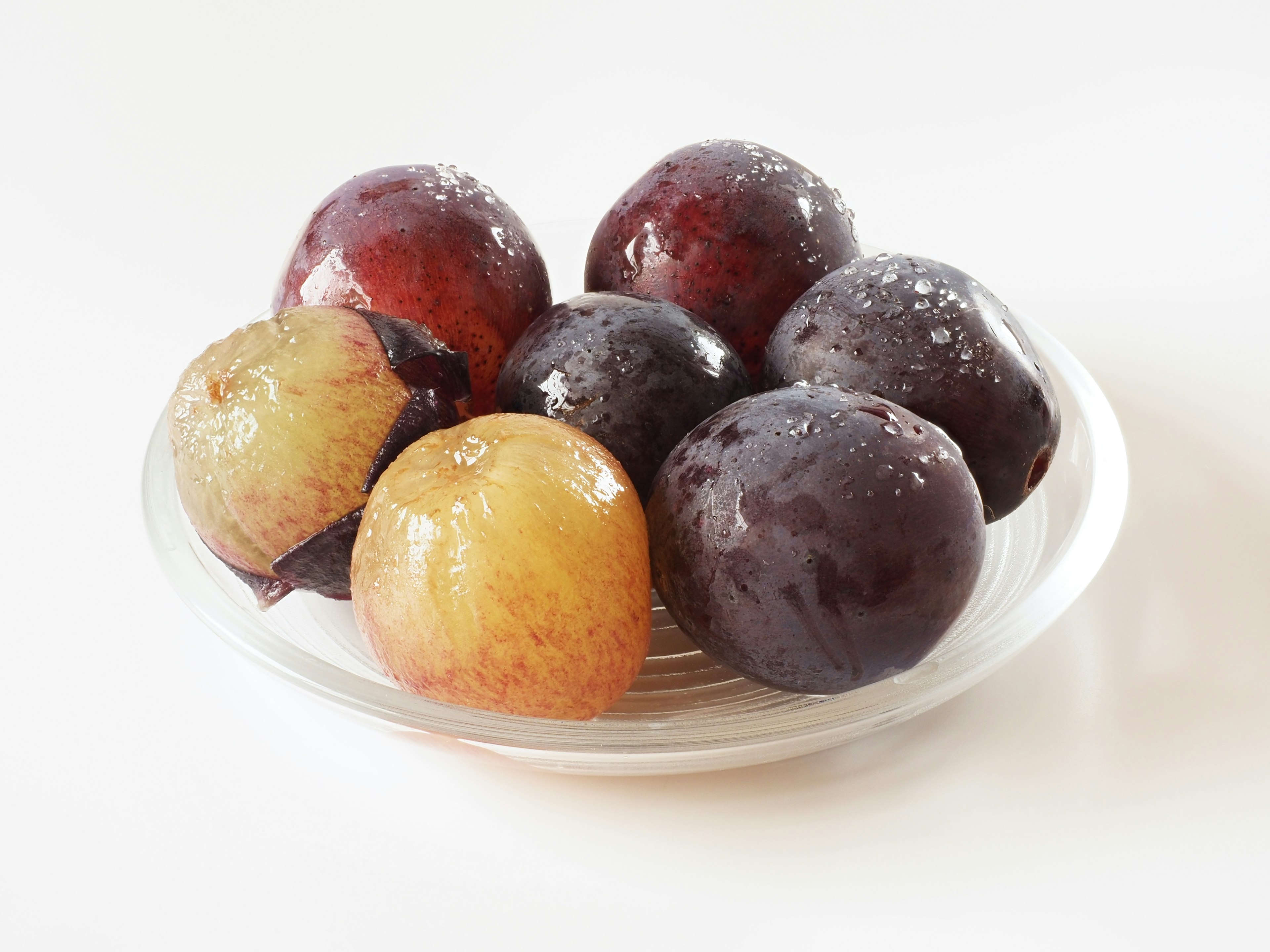 A variety of colorful plums arranged on a clear plate