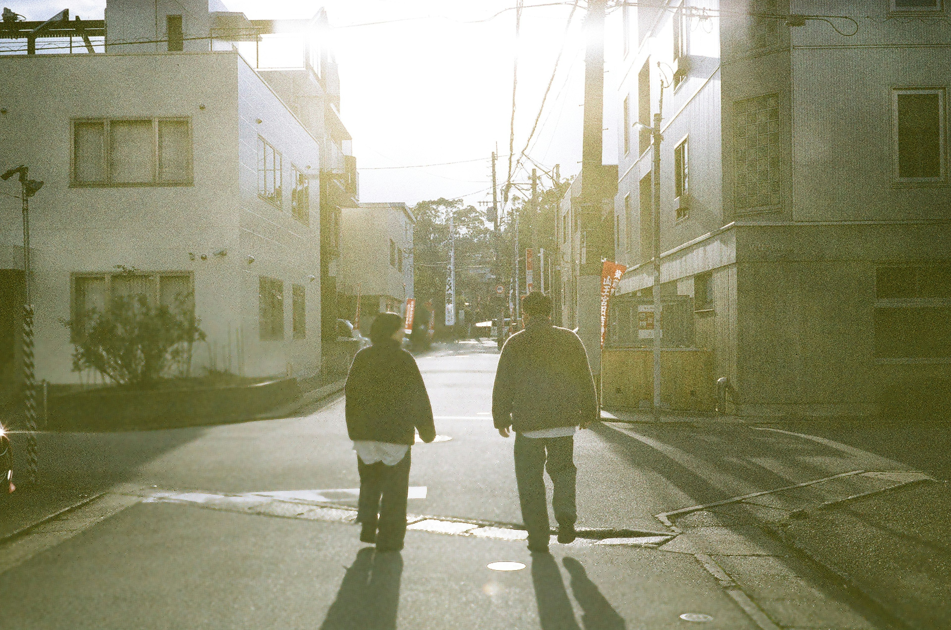 Two people walking down a street with the sun behind them