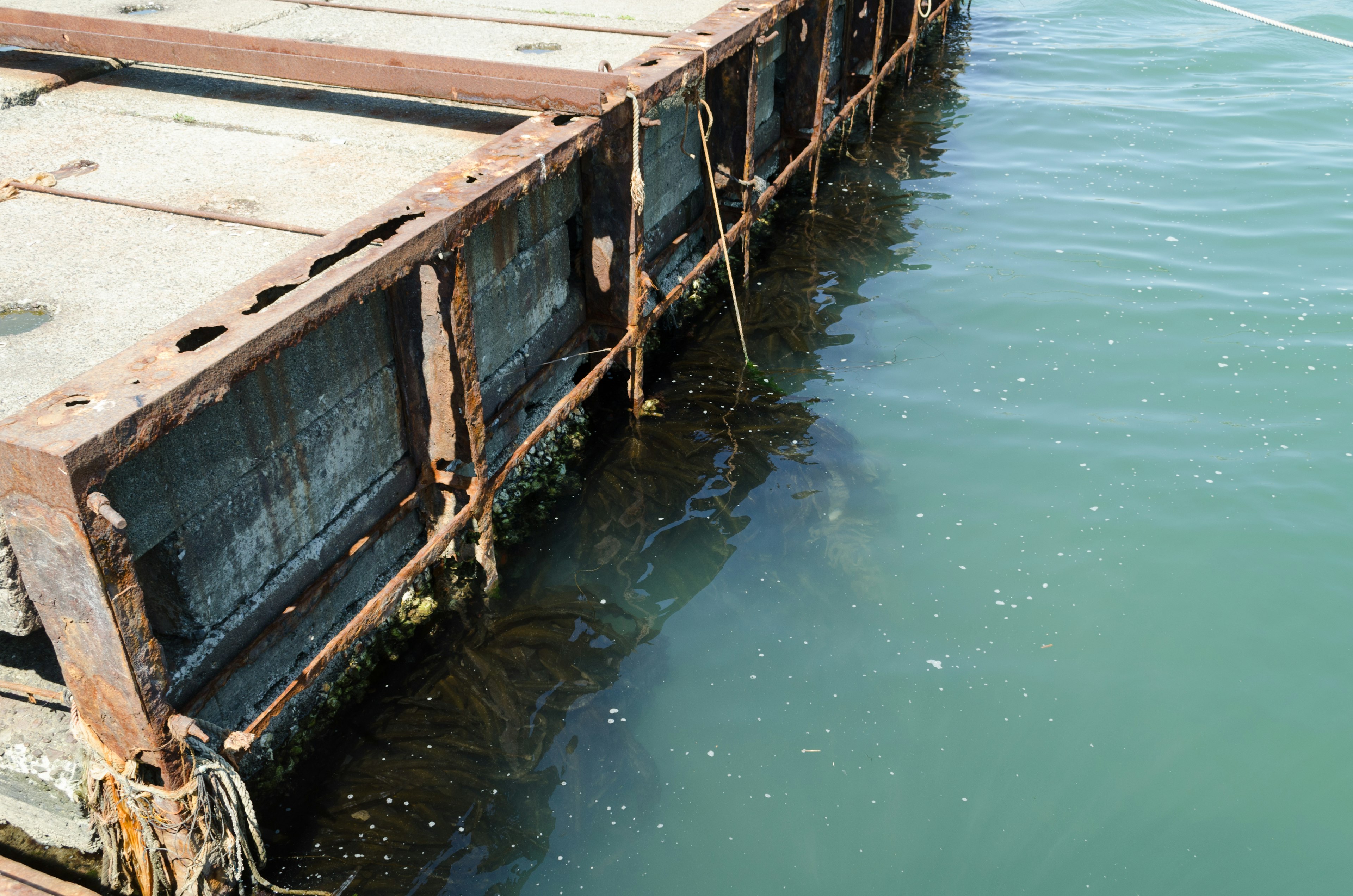 Bagian dari dermaga tua dengan logam berkarat dan permukaan air