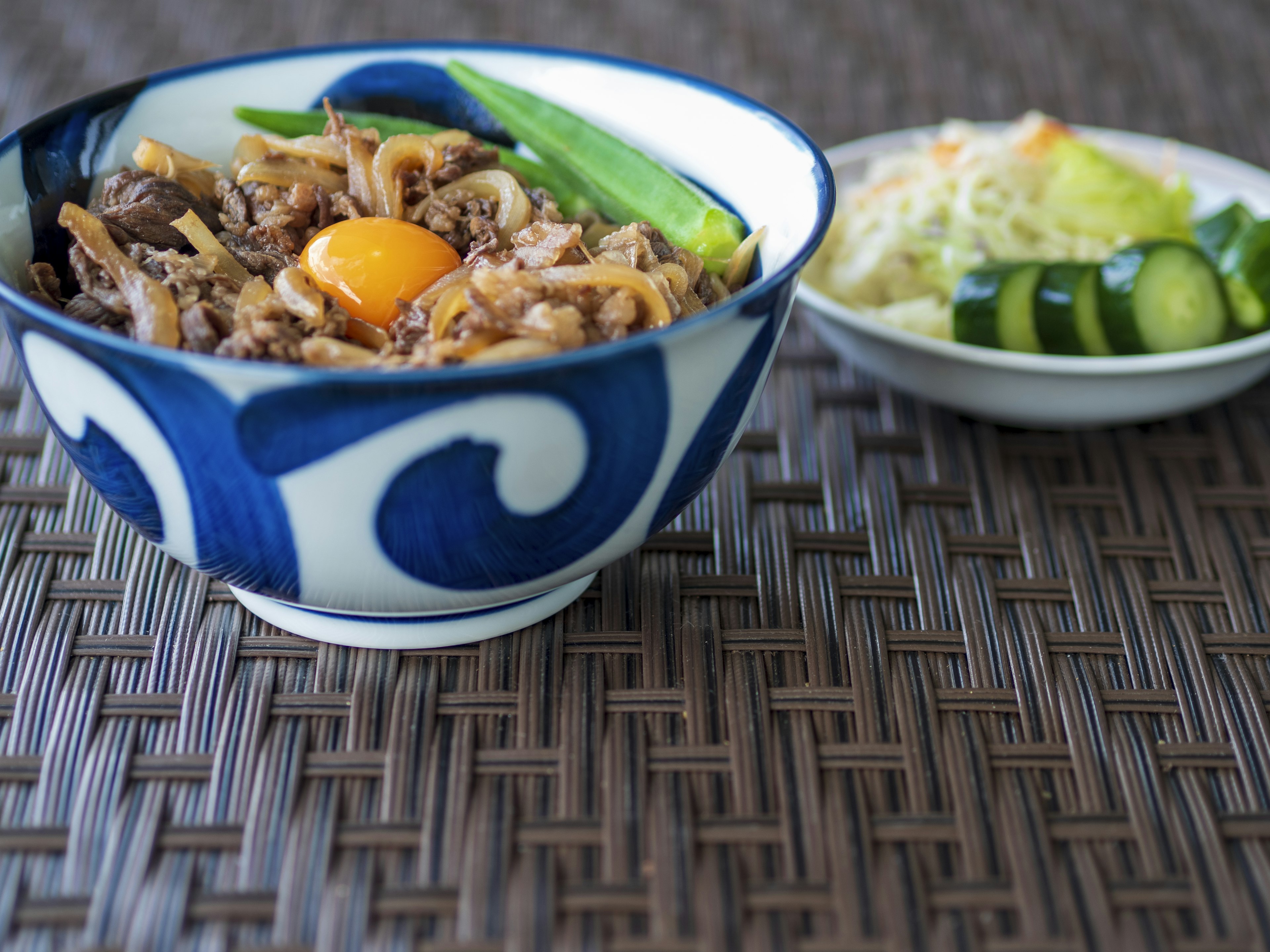 A bowl with blue patterns filled with rice and egg yolk alongside a side of vegetables