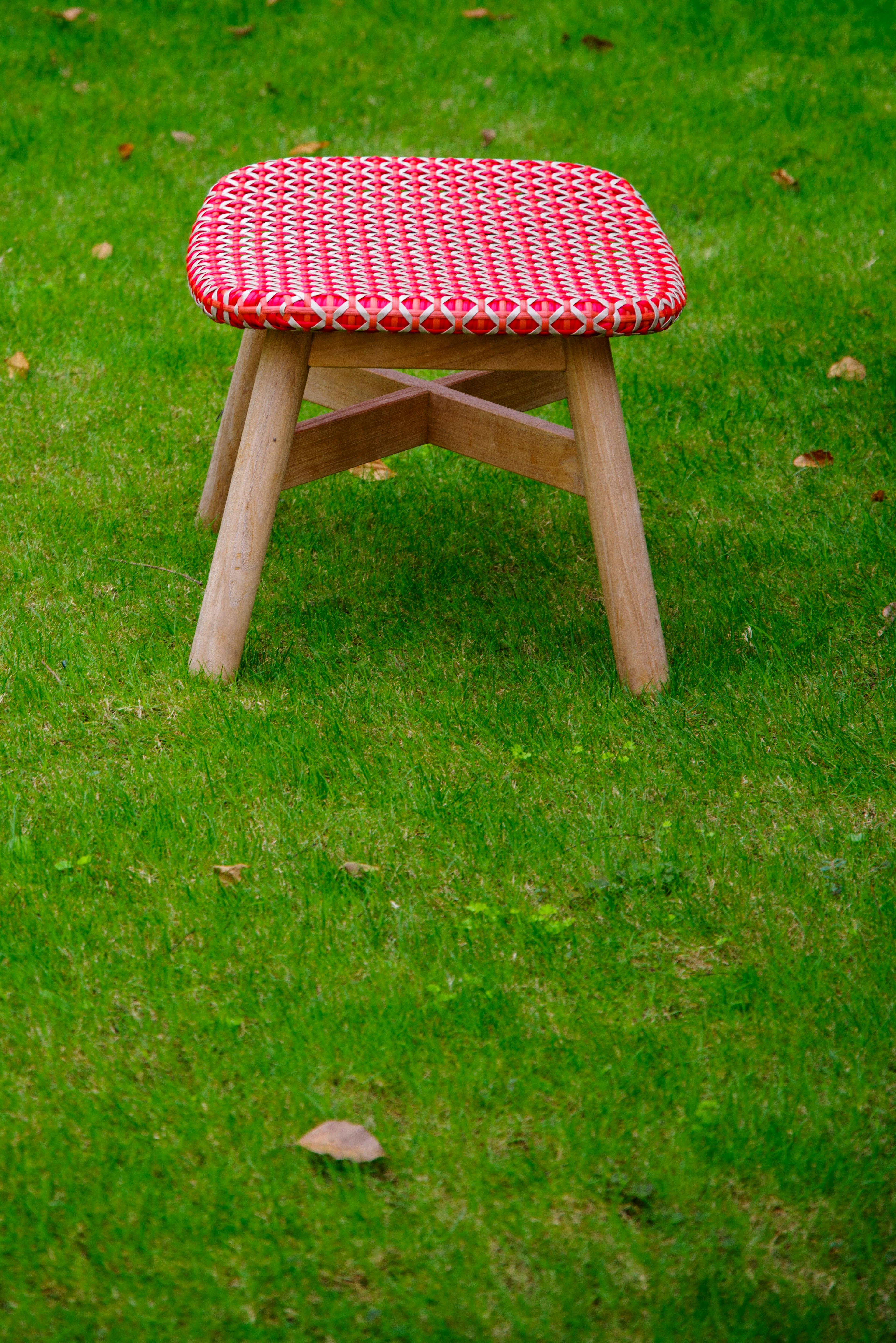 Kursi kayu dengan bantal kotak merah di atas rumput hijau