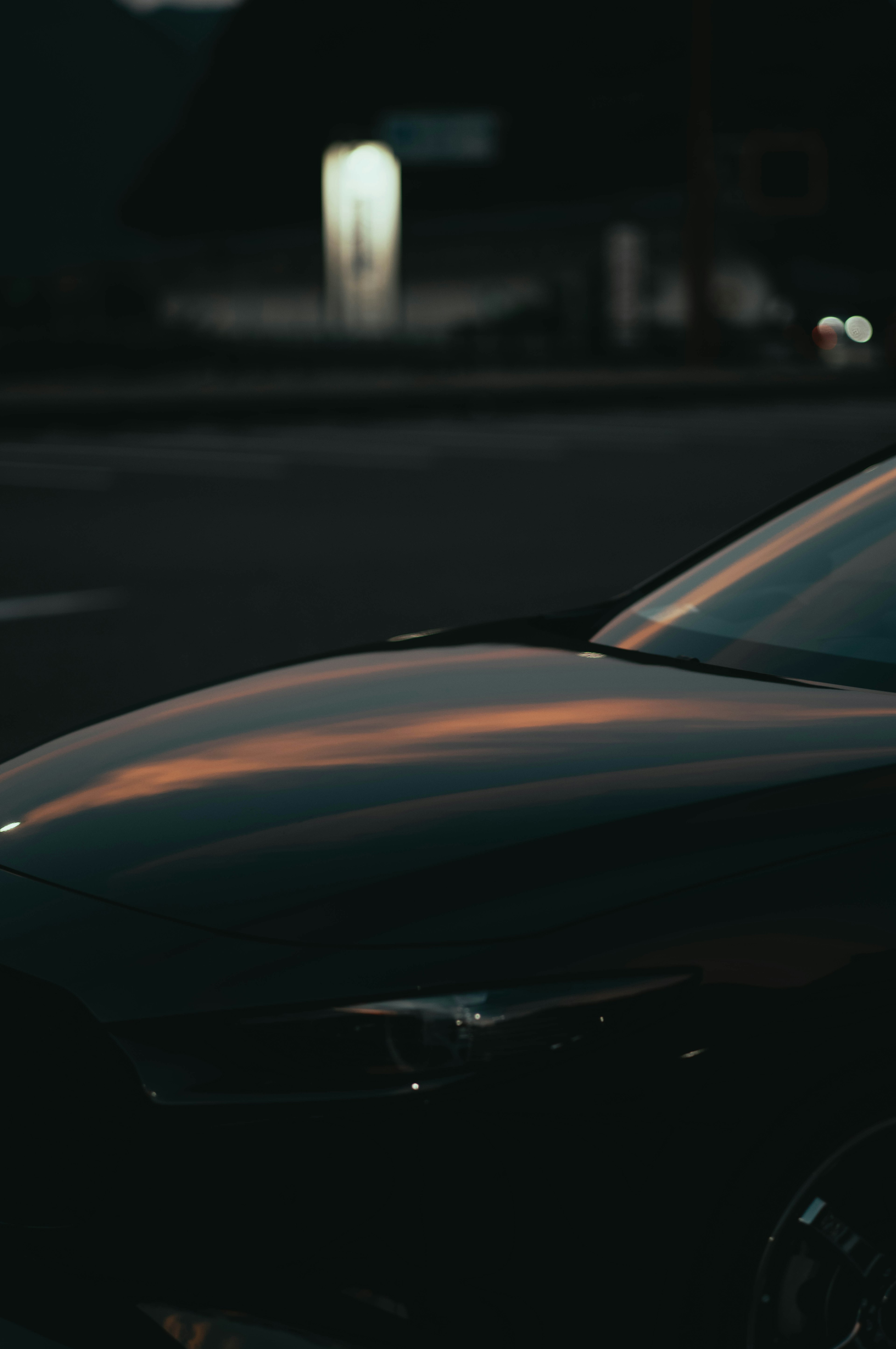 Nahaufnahme der Motorhaube eines schwarzen Autos, das Licht auf einem dunklen Hintergrund reflektiert