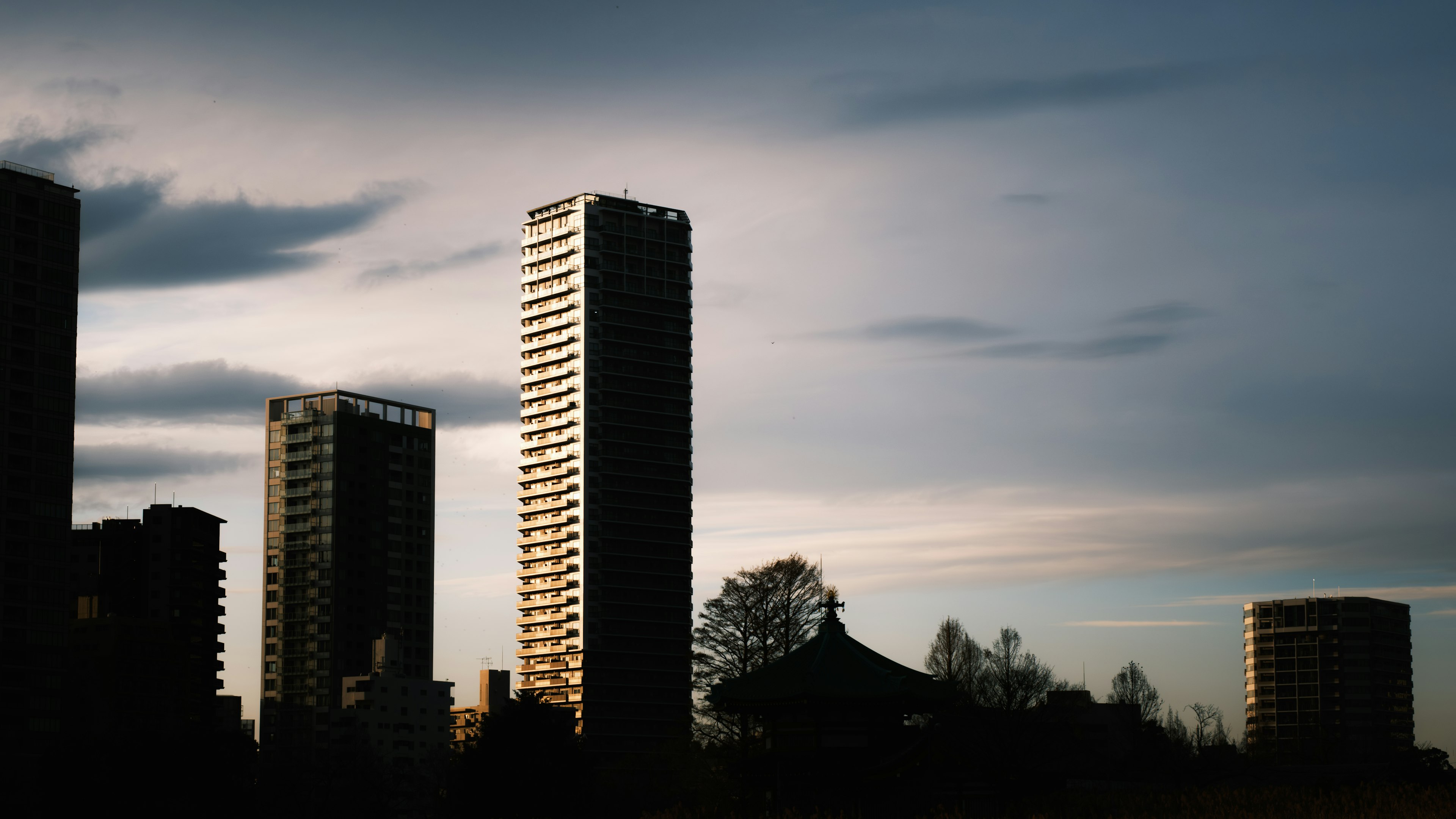 Silhouette of a city at dusk featuring high-rise buildings and a cloudy sky