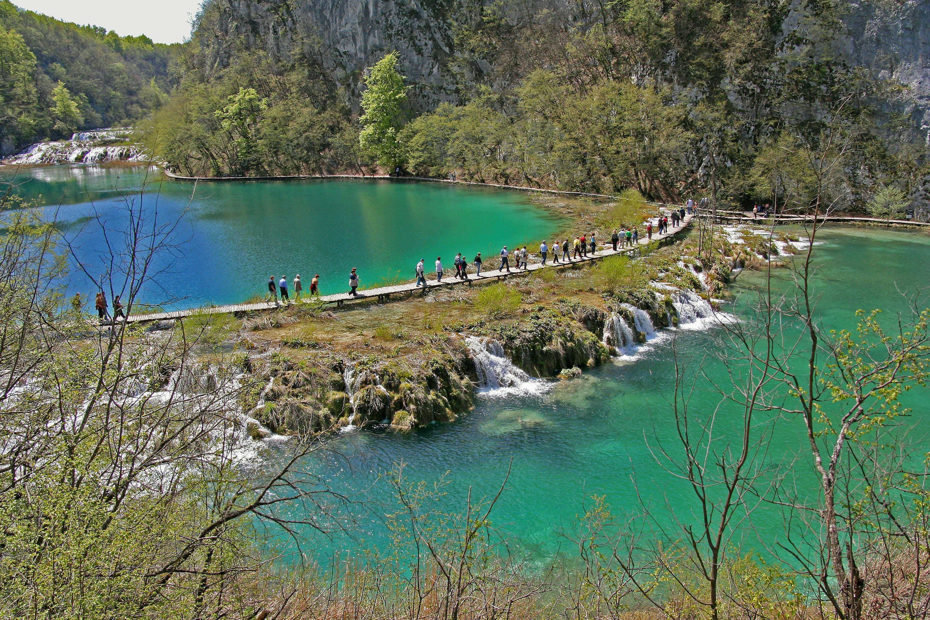 Vue pittoresque de lacs turquoise avec un sentier et des touristes marchant le long des chutes d'eau