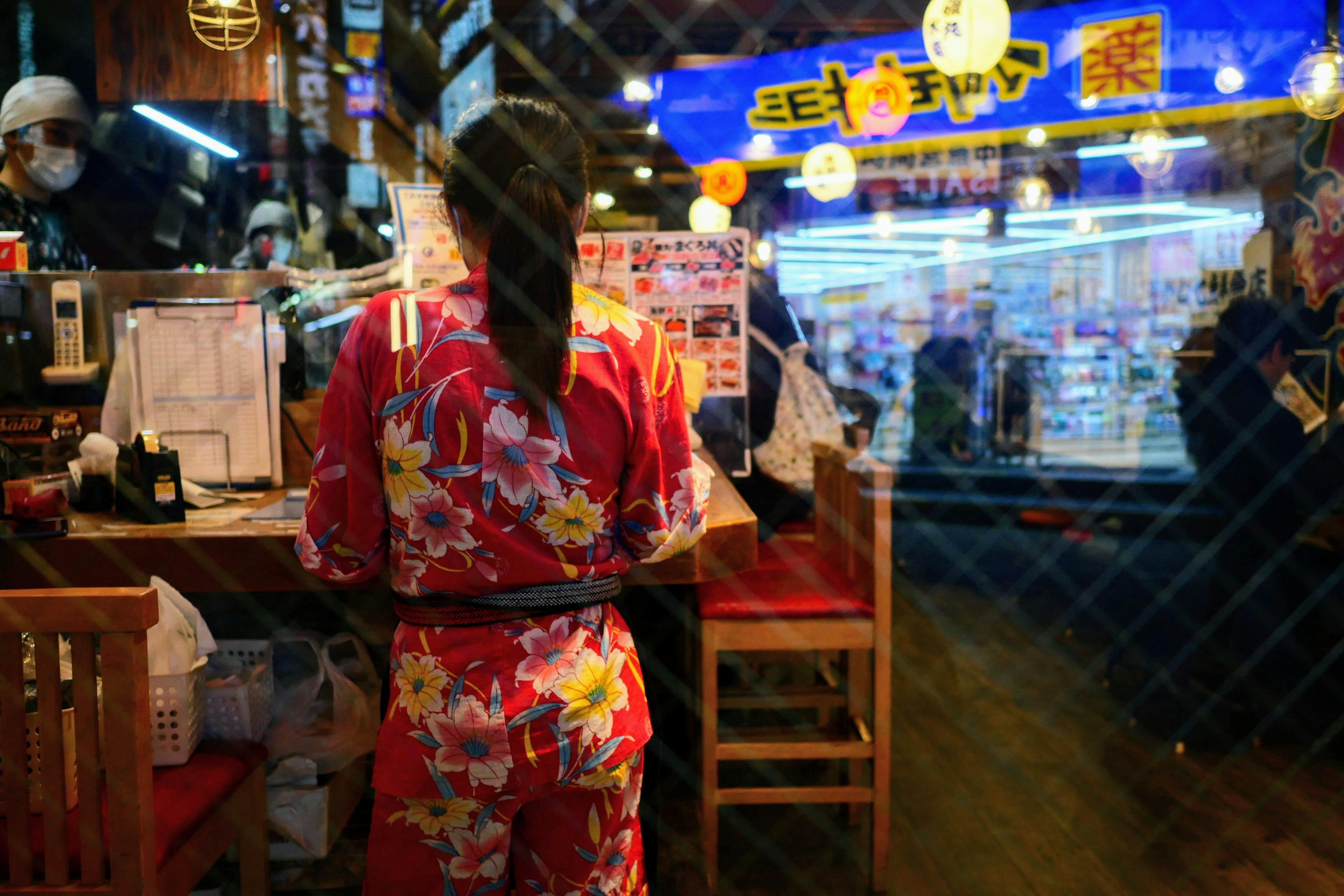 Seorang wanita berpakaian kimono berwarna-warni sedang menyiapkan makanan di sebuah kios