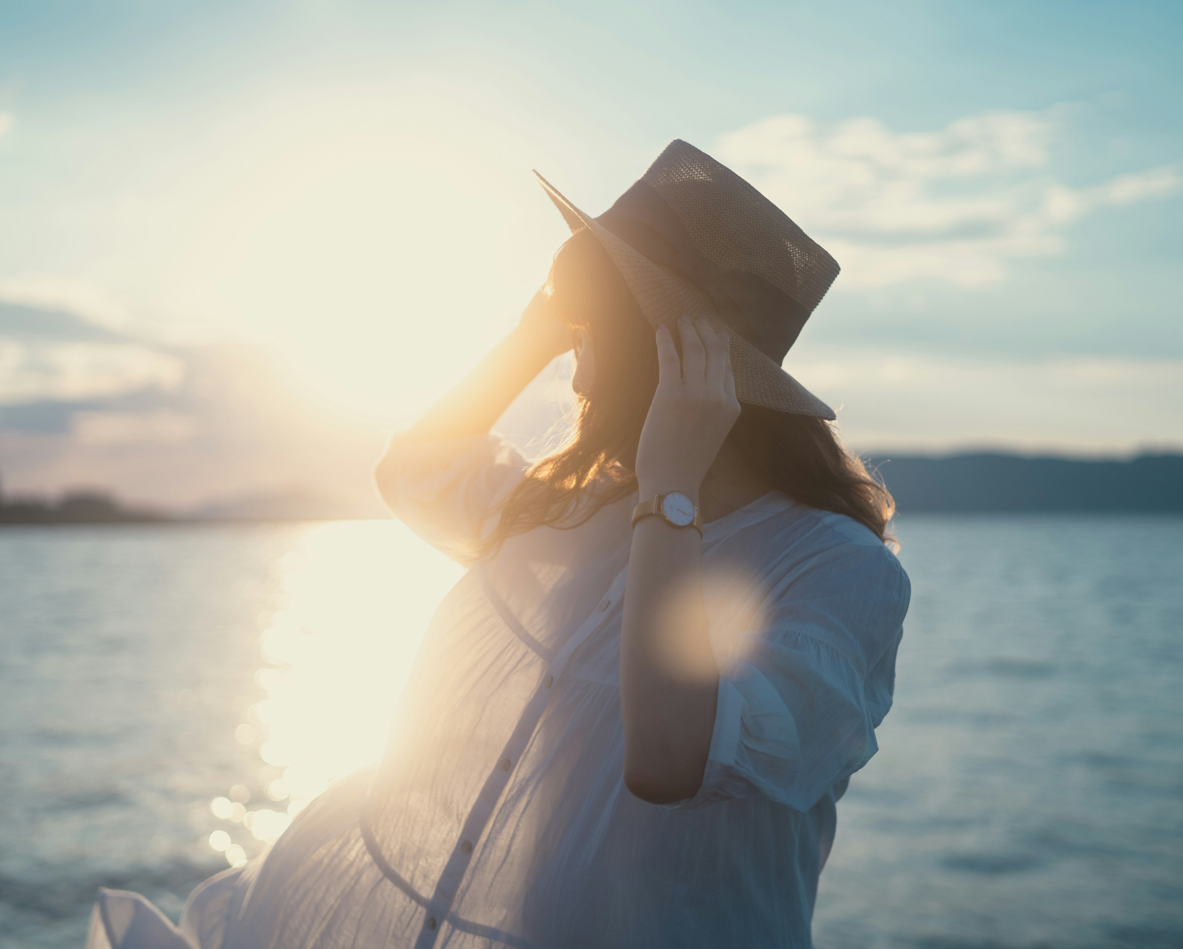 海辺で帽子をかぶった女性のシルエットが日差しを浴びている