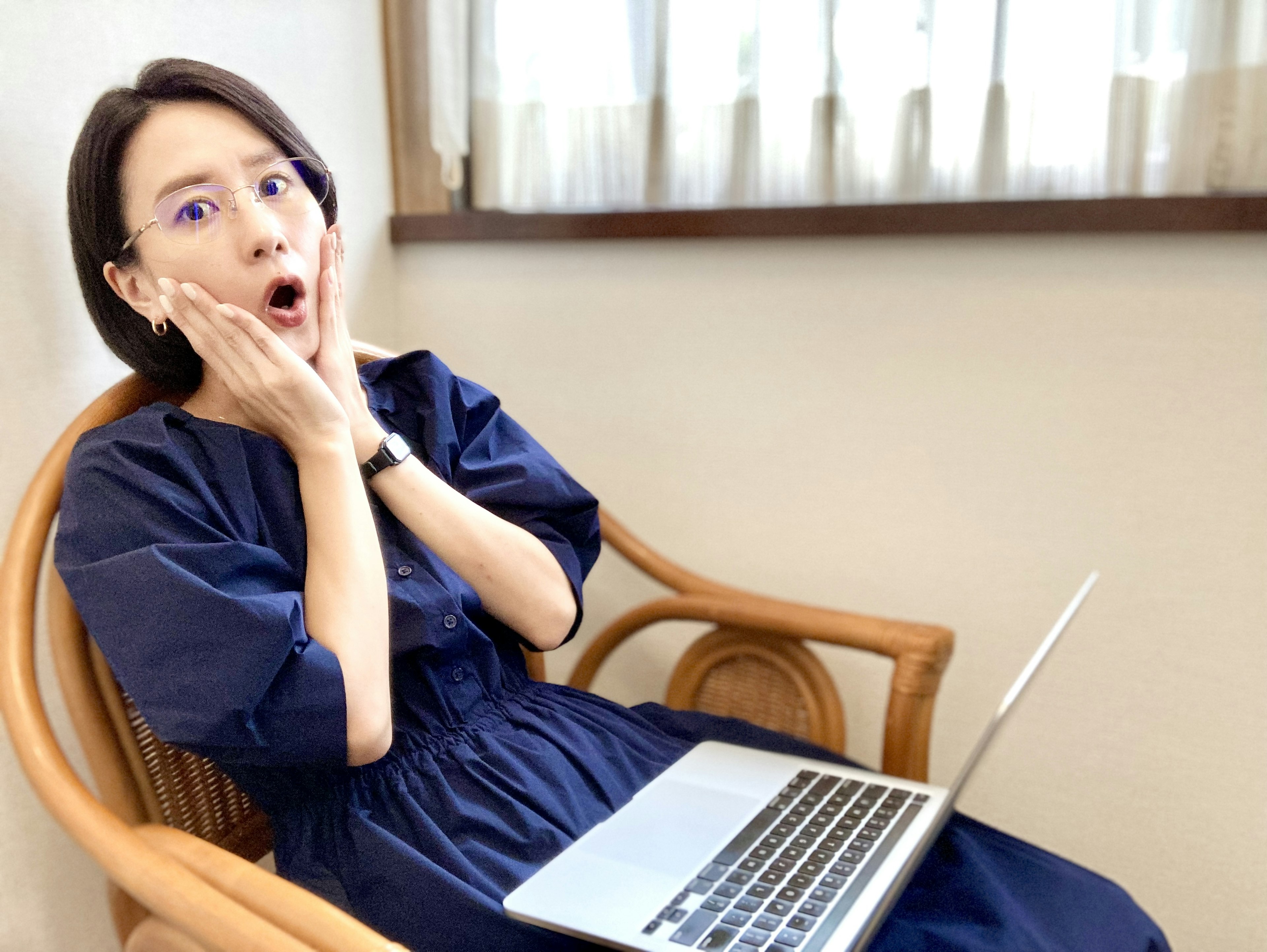 A surprised woman sitting in a chair looking at a laptop