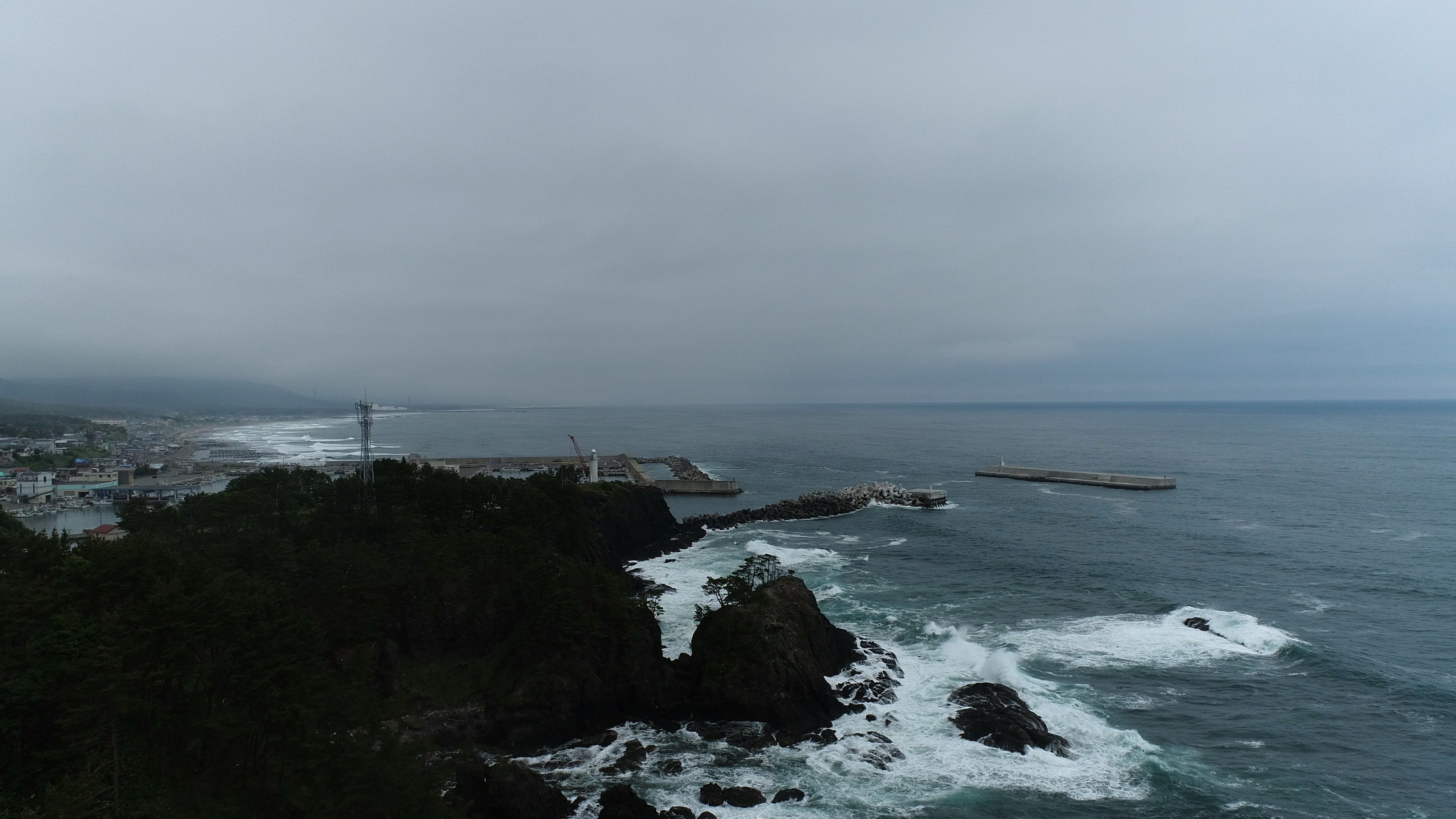 海岸景觀岩石海岸和拍打浪潮陰天和遠處的燈塔