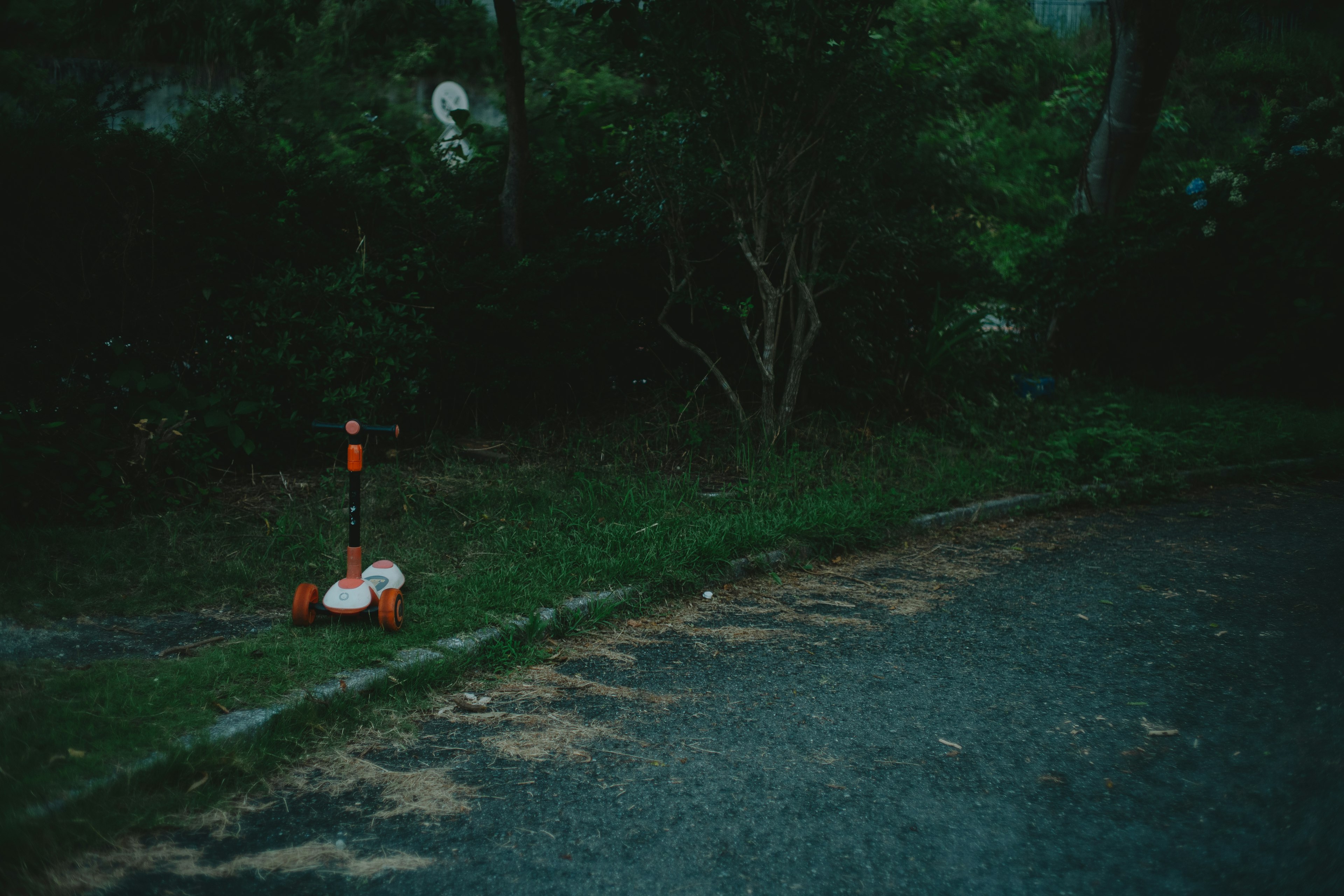 Una escena oscura de parque con un patinete naranja y blanco colocado en el césped