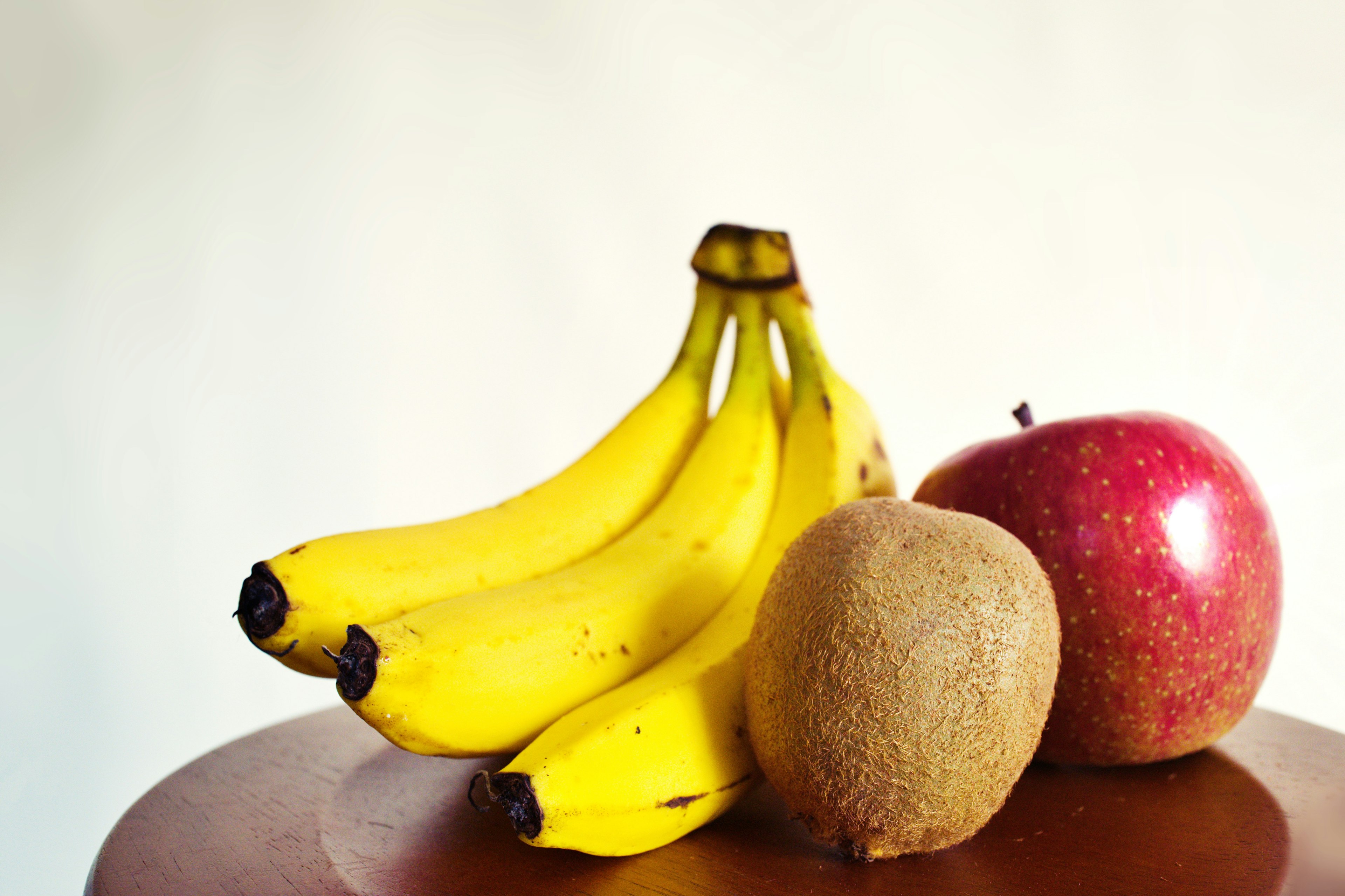 Sekumpulan pisang kuning sebuah apel merah dan kiwi coklat di atas meja kayu