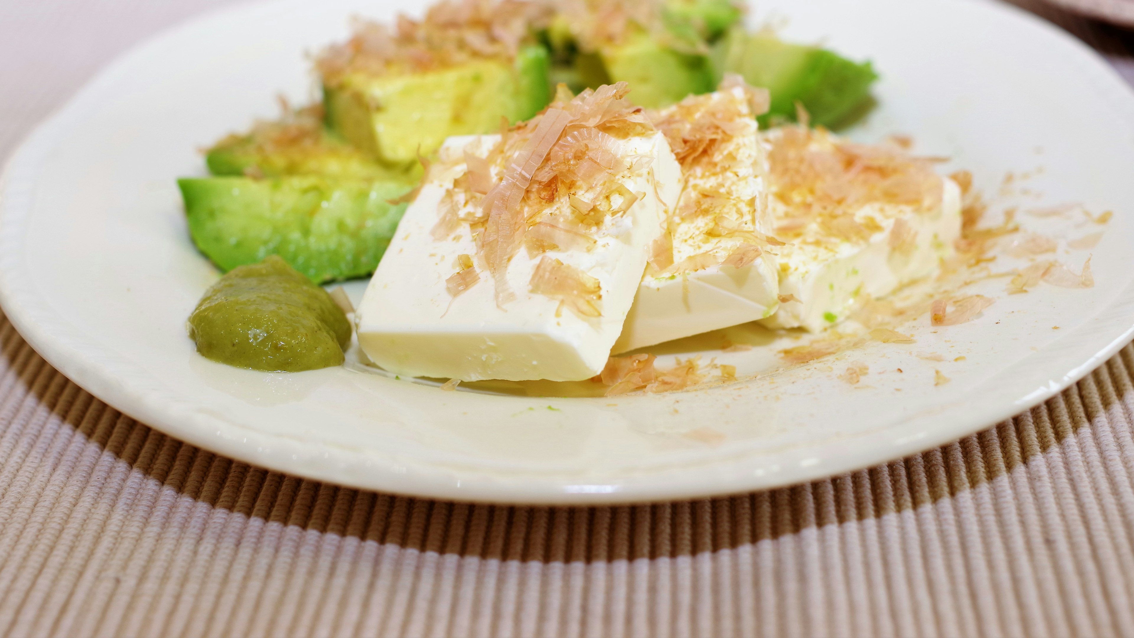 A dish featuring avocado slices and tofu garnished with bonito flakes on a white plate