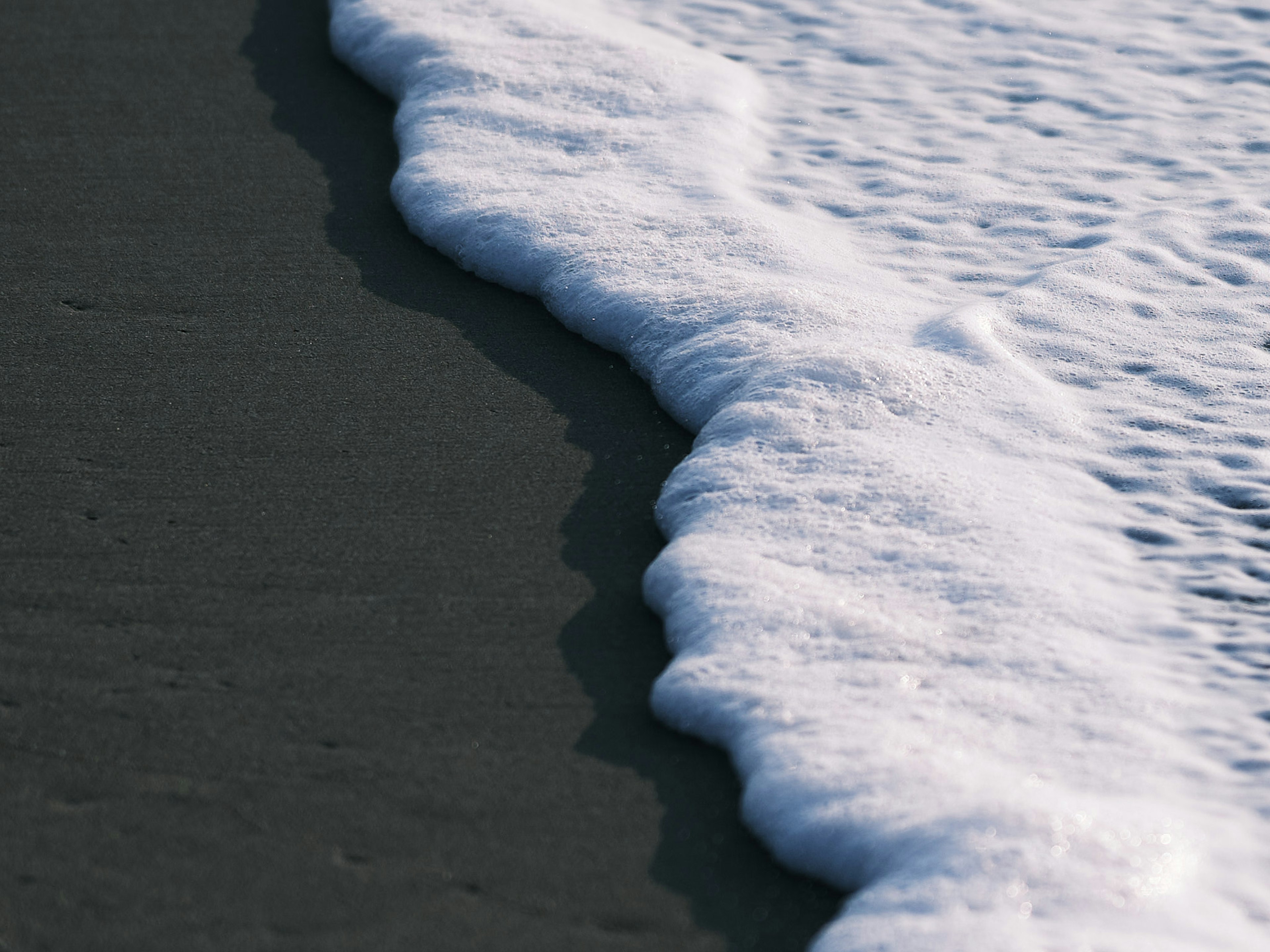 Vague mousse blanche se lavant sur la plage de sable sombre