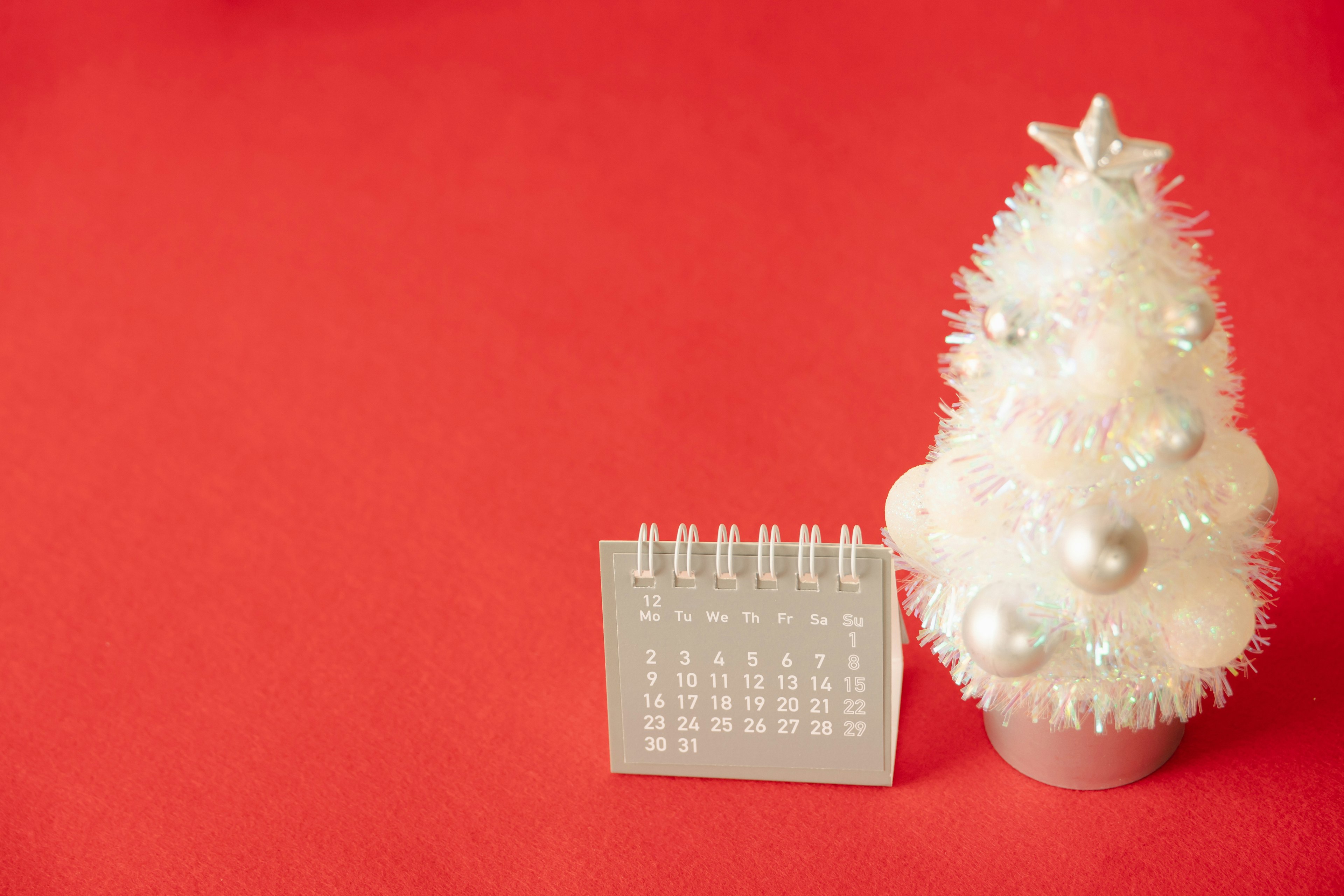 Árbol de Navidad blanco junto a un calendario sobre un fondo rojo