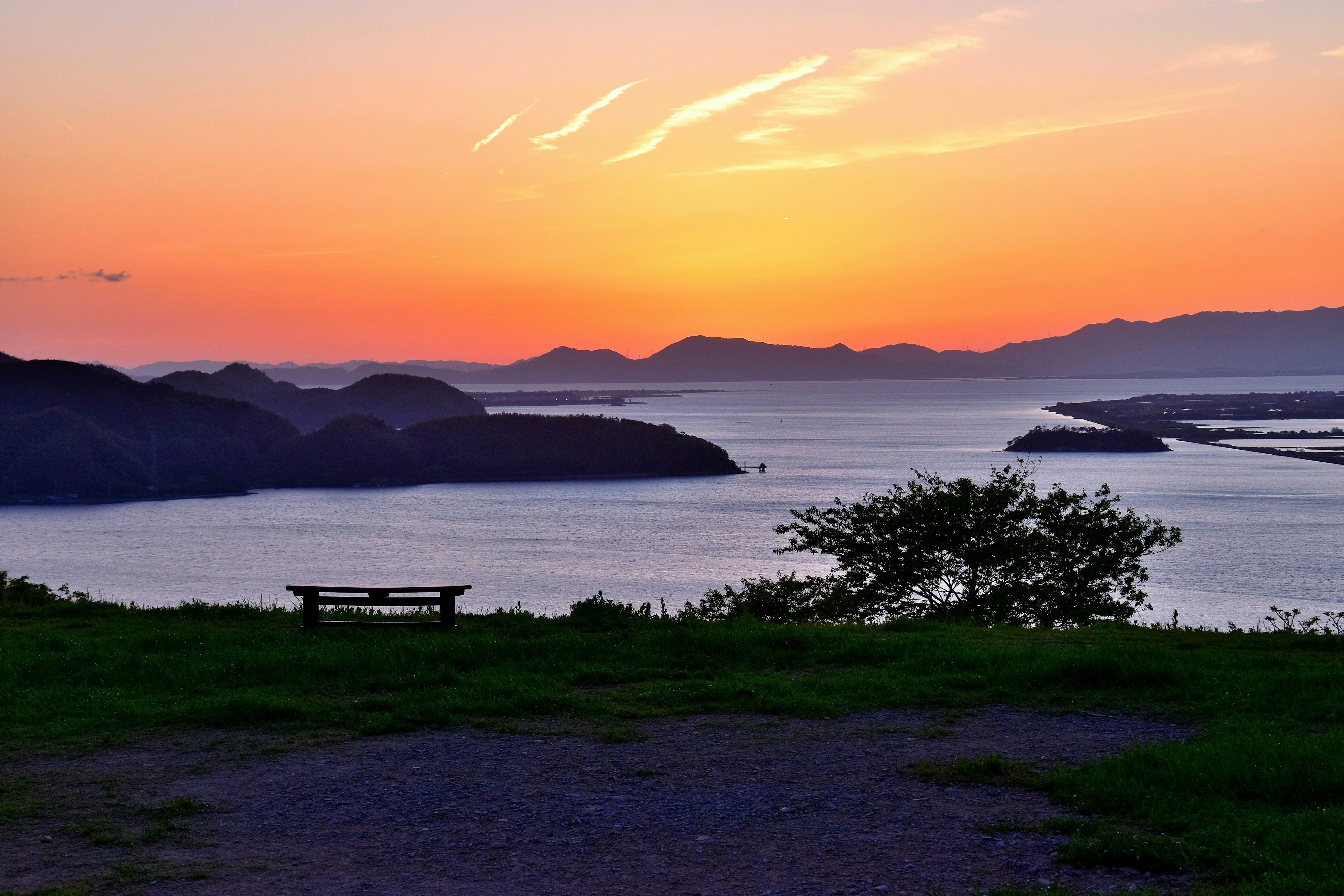 美しい夕日が沈む海の景色 ベンチと緑の草地が見える