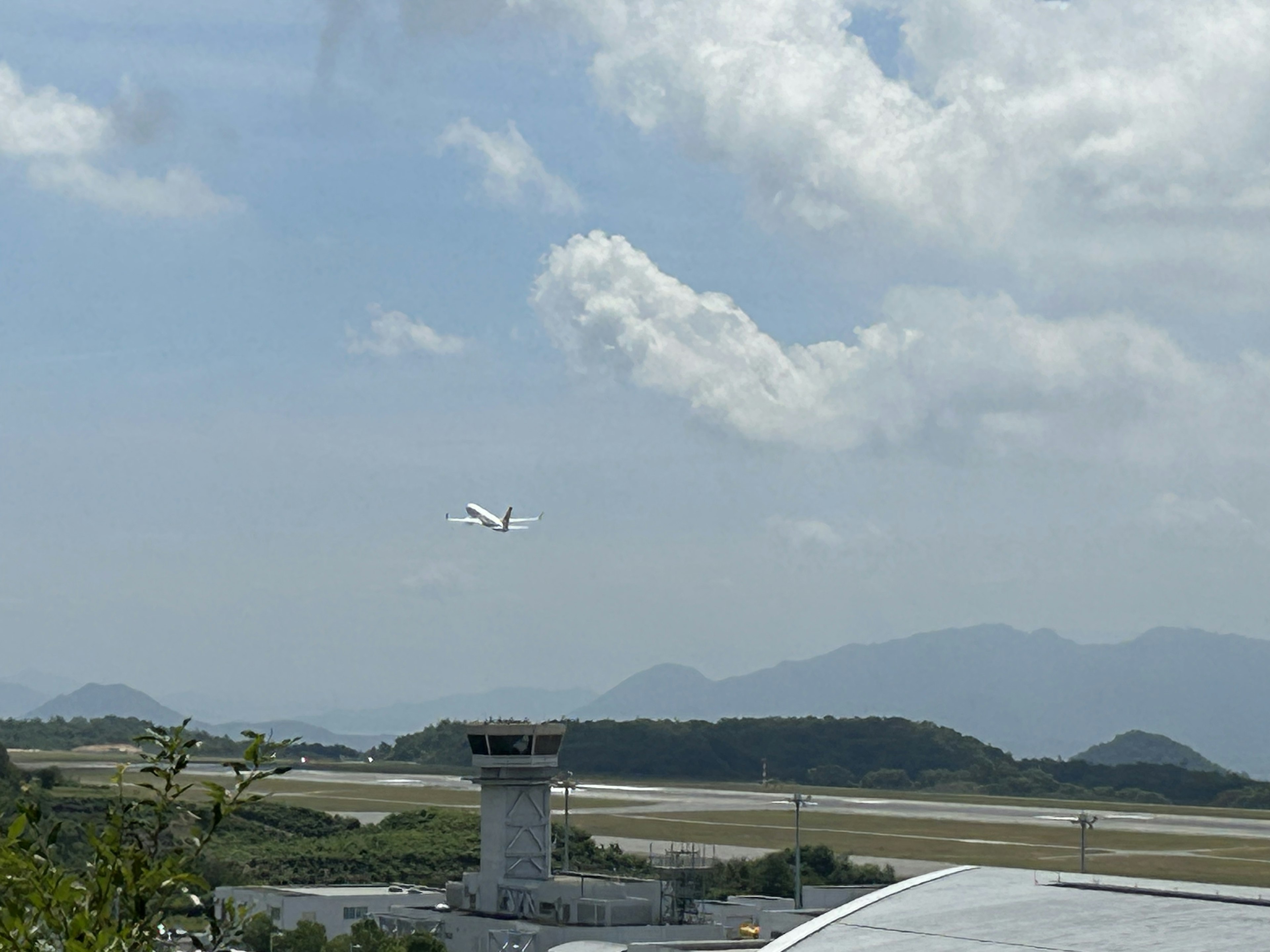 Ein Flugzeug startet mit einem Flughafenturm und Bergen im Hintergrund