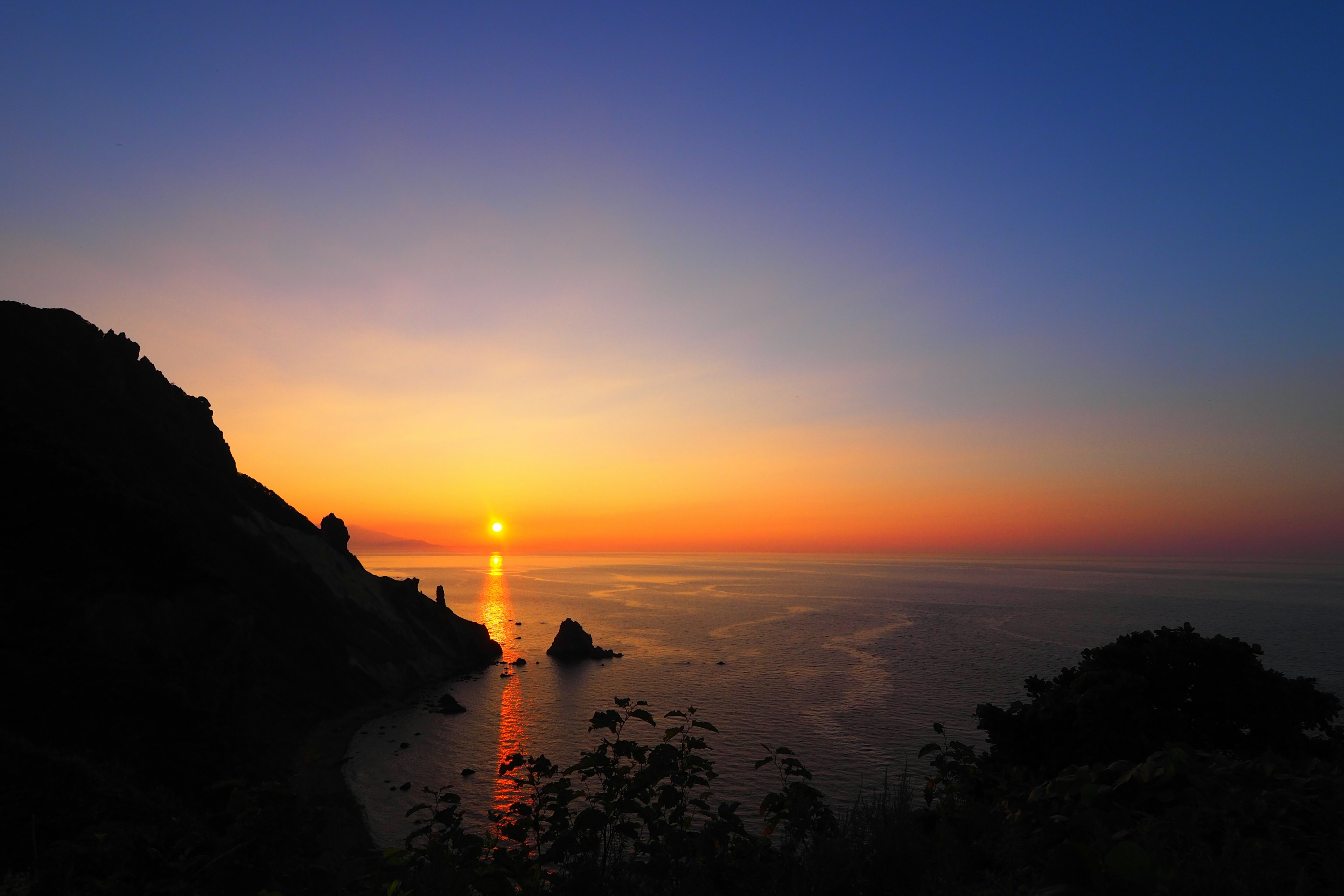 A beautiful sunset over the ocean with silhouettes of rocks and plants