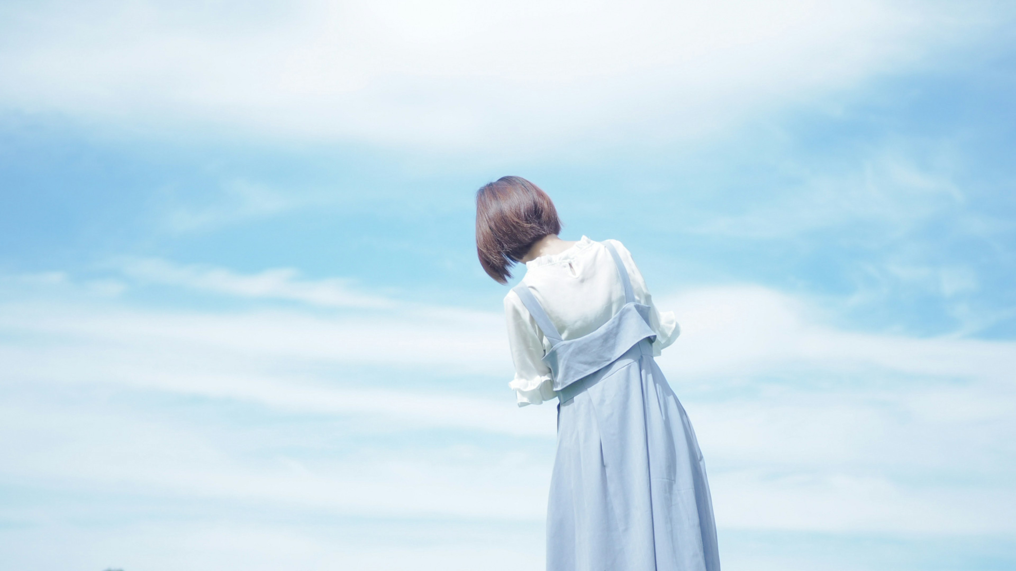 Una mujer con un vestido claro mirando hacia atrás bajo un cielo azul