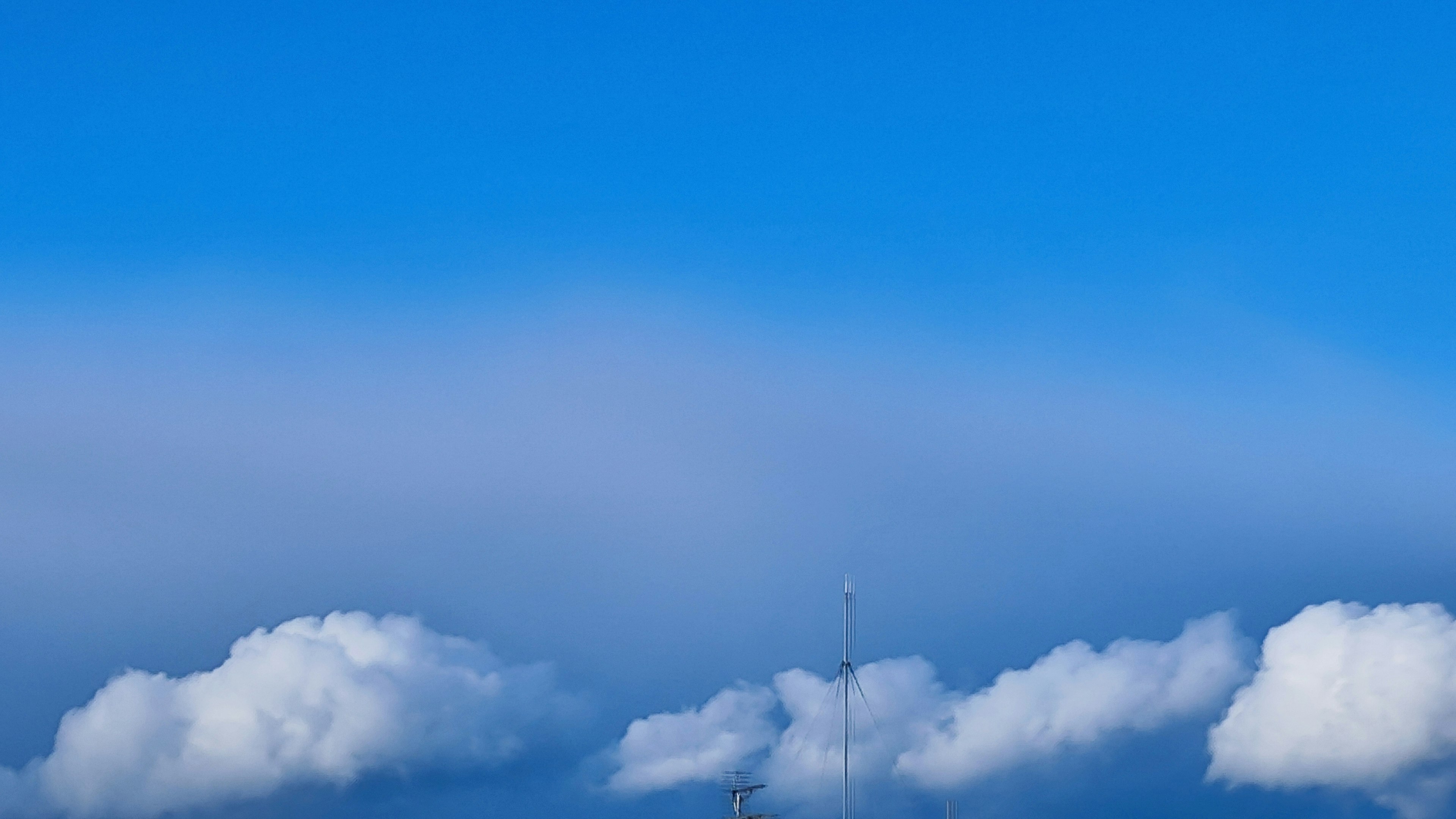 Awan putih melayang di langit biru dengan menara di bawahnya