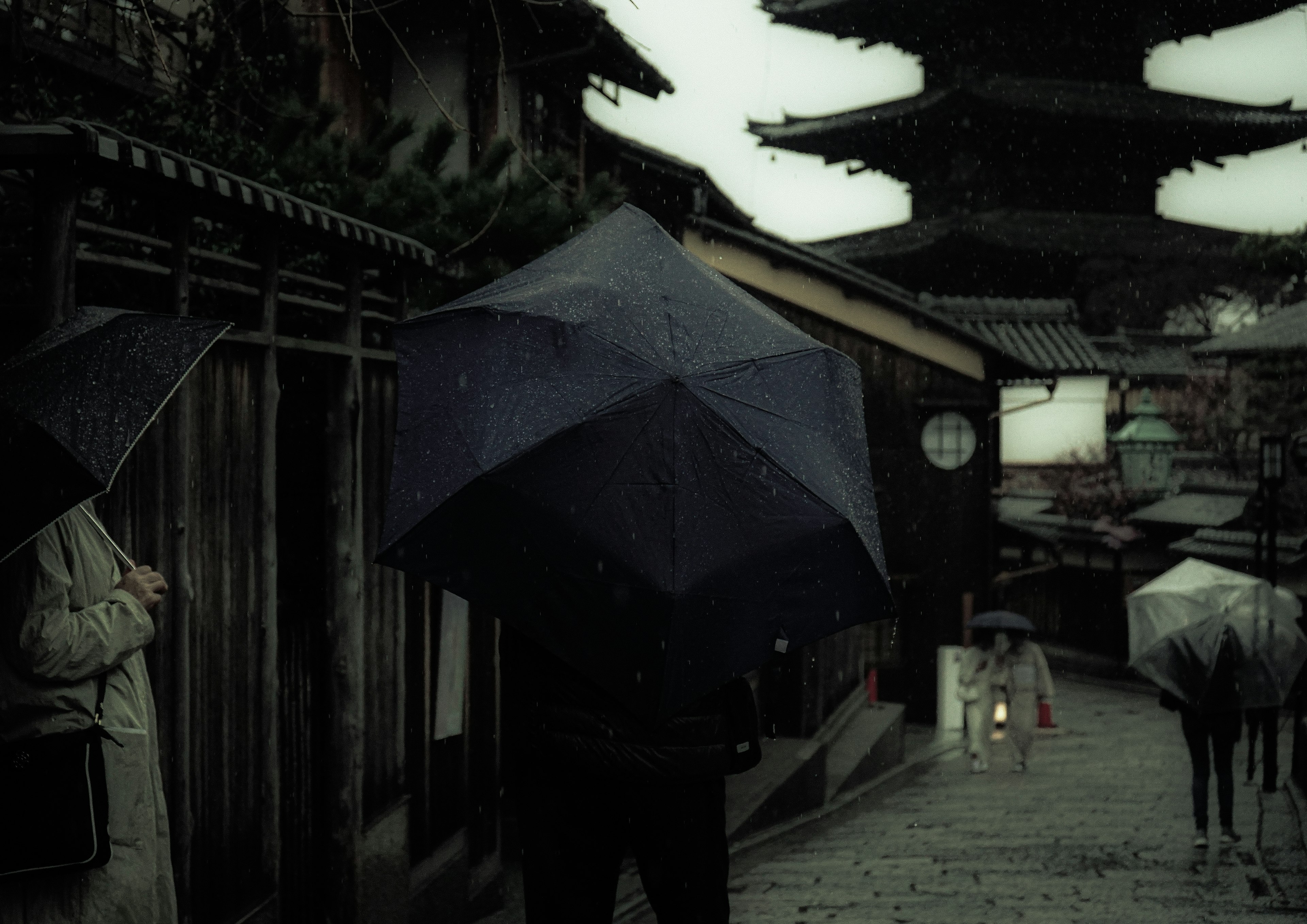 雨の中の傘を持つ人々が歩く古い街並み