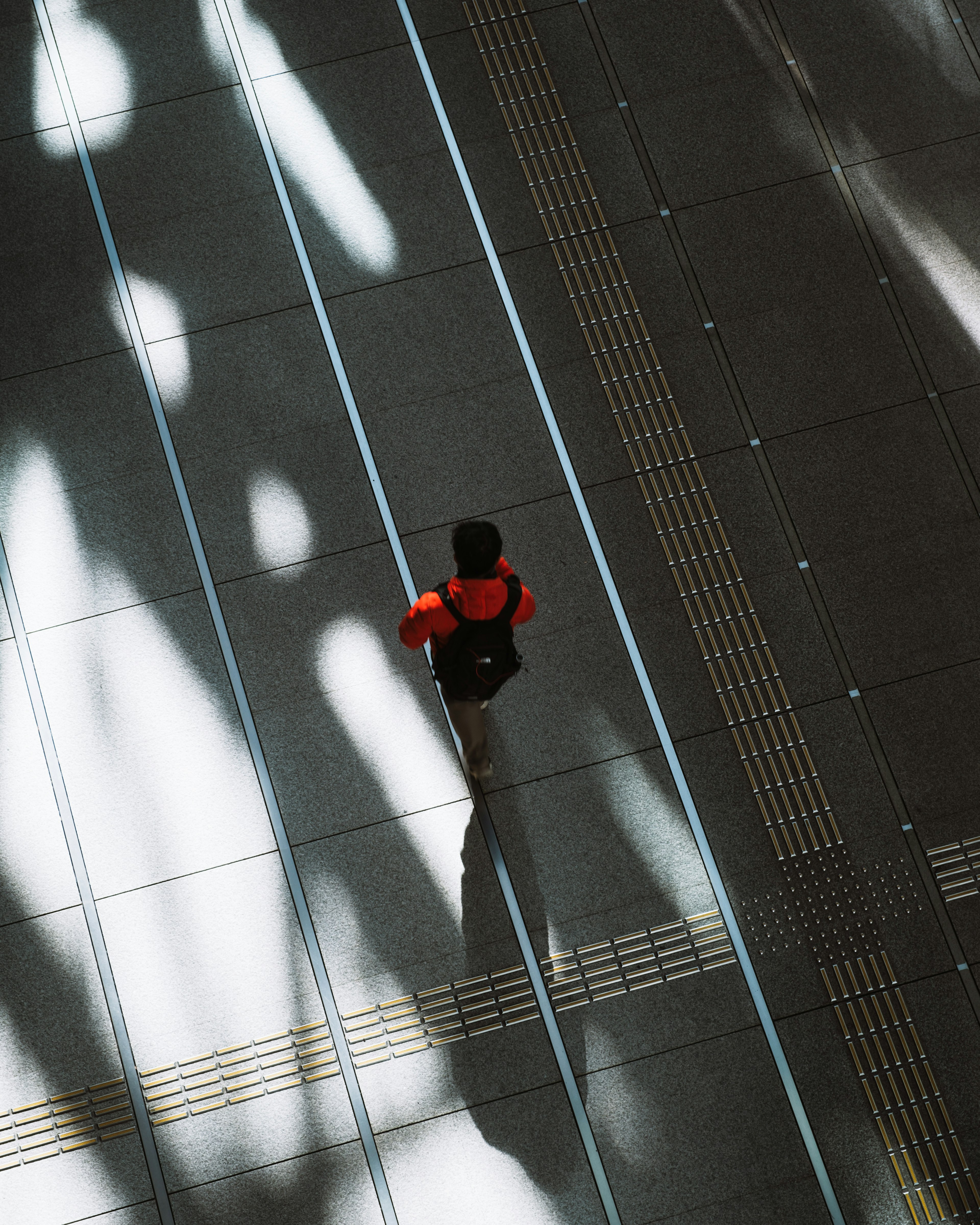 Une personne portant une chemise rouge marchant sur un sol lumineux avec des ombres