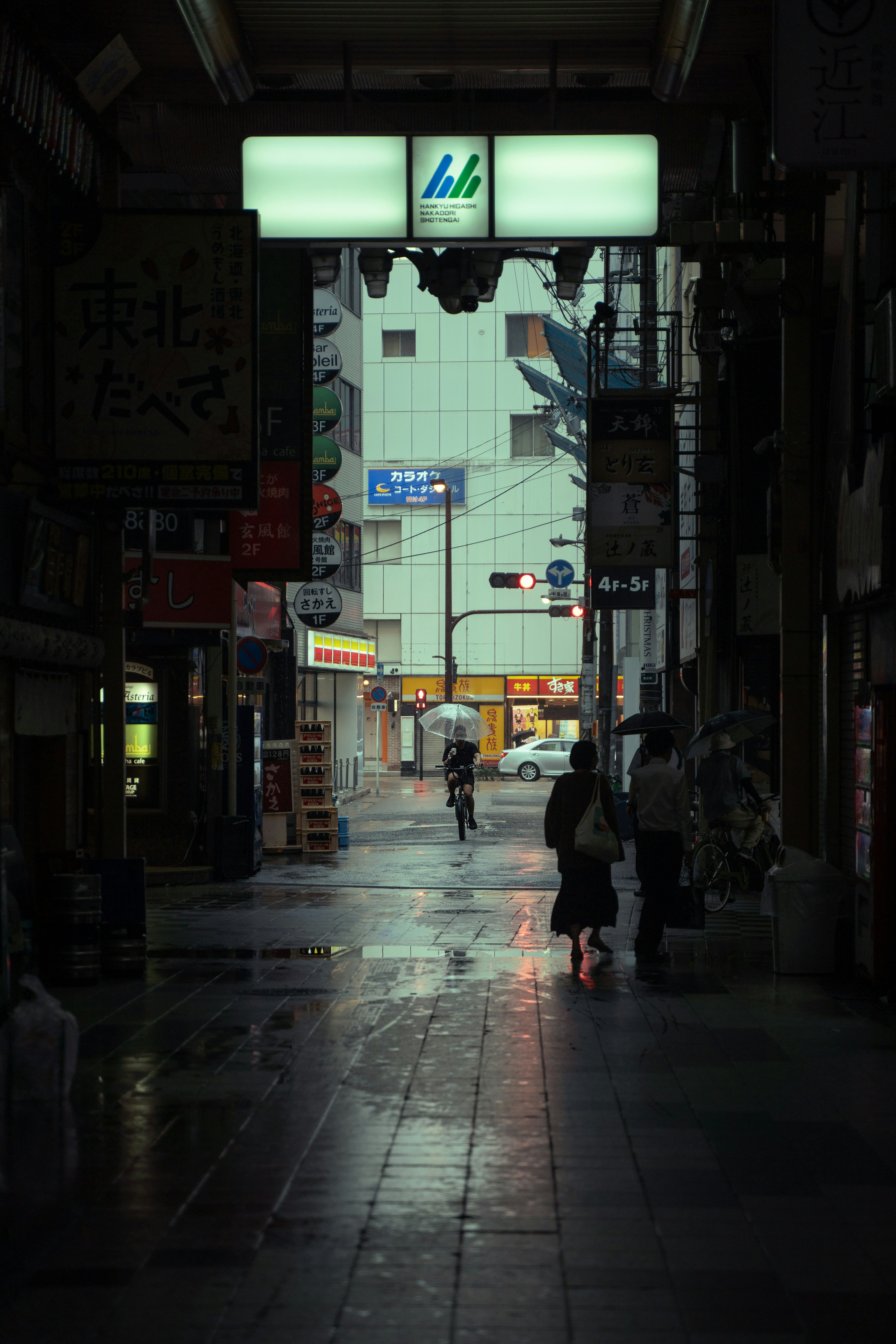 在昏暗街道上站立的人影，雨水坑反射著光