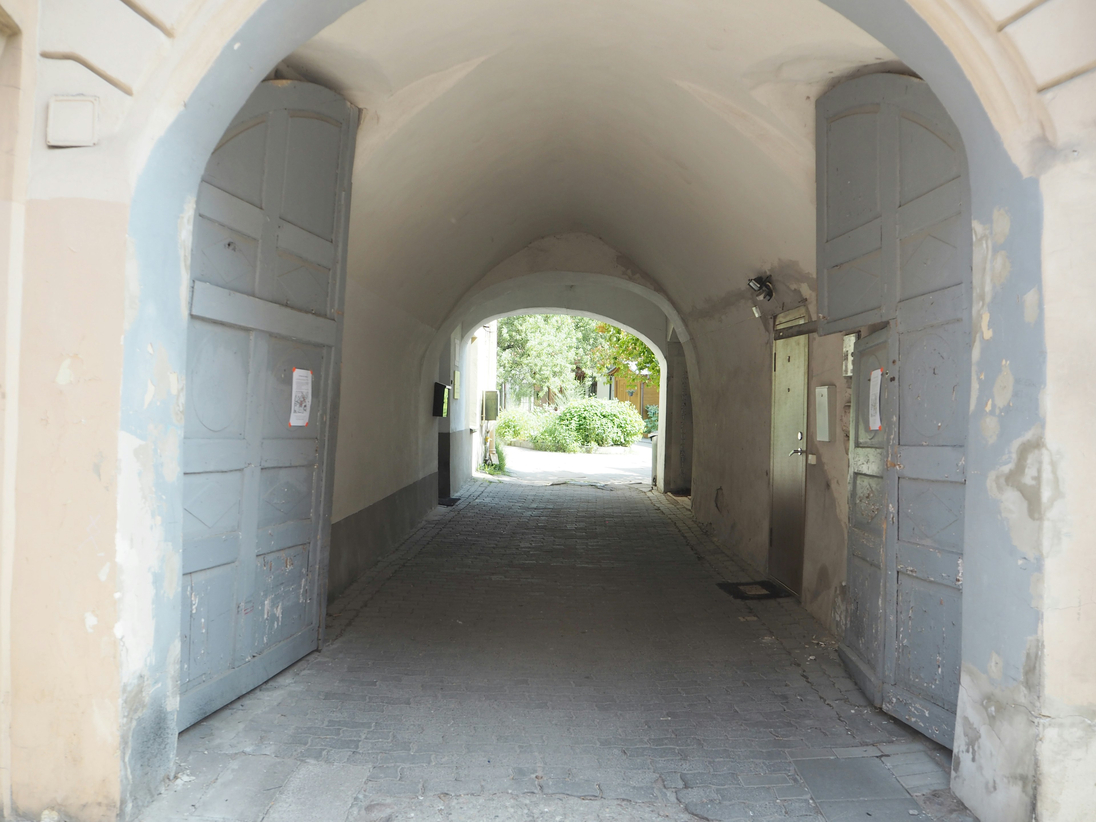 Arco que conduce a un jardín verde con muros y puertas desgastadas