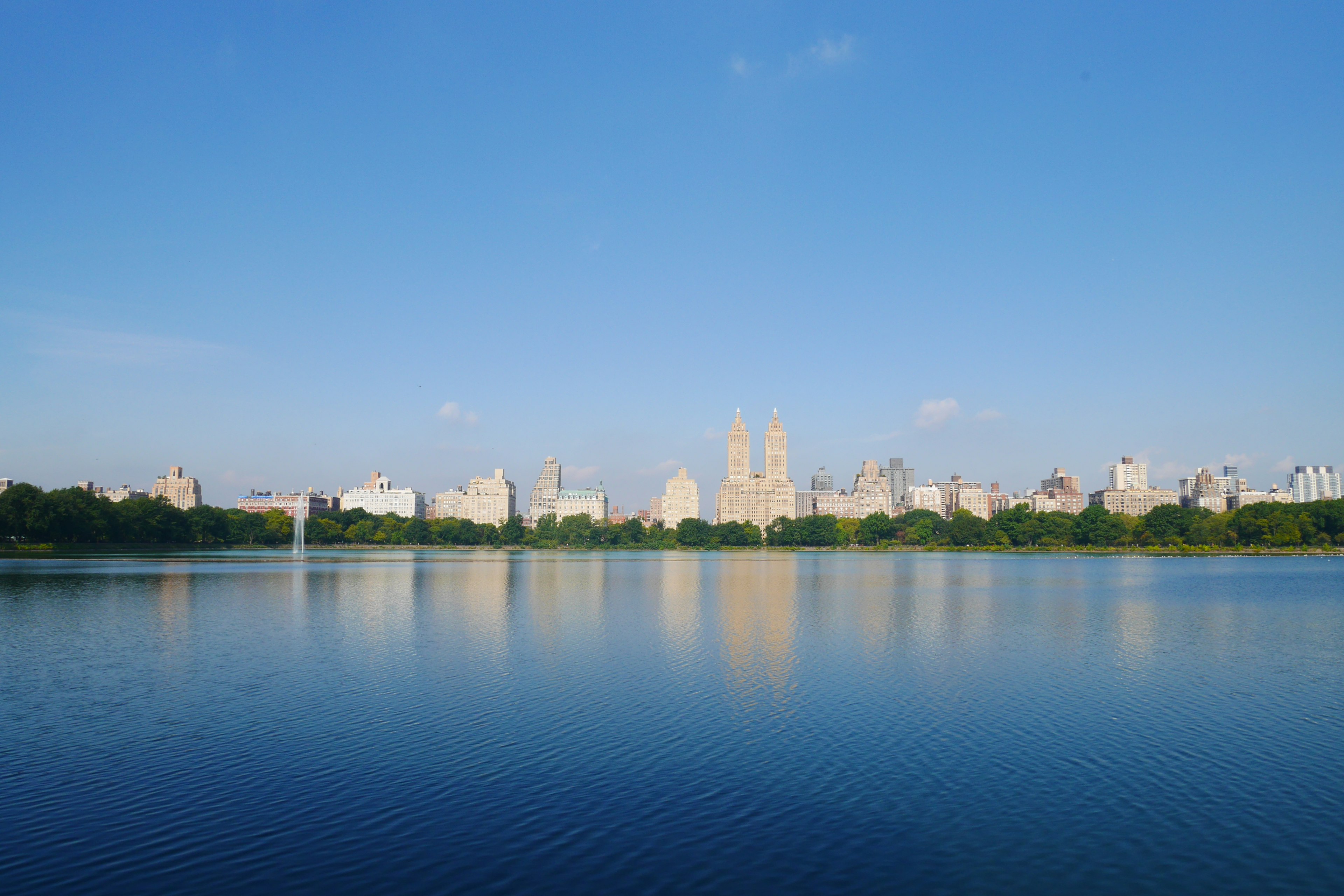 A serene lake reflecting a city skyline under a clear blue sky