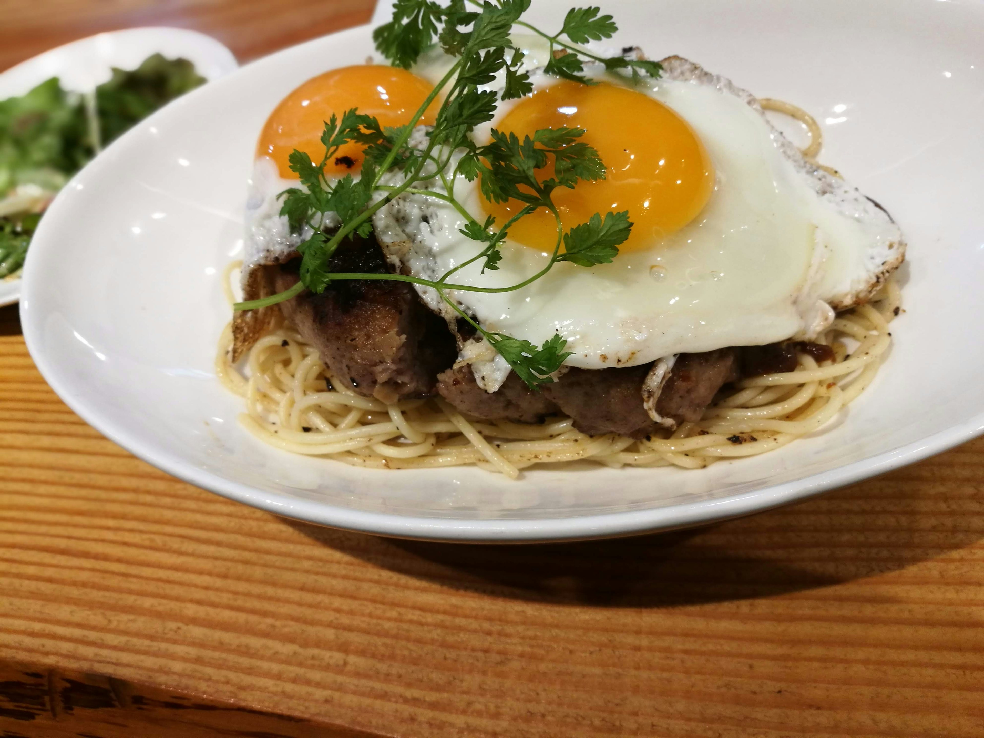 Une assiette de spaghetti surmontée de deux œufs et de viande garnie de coriandre