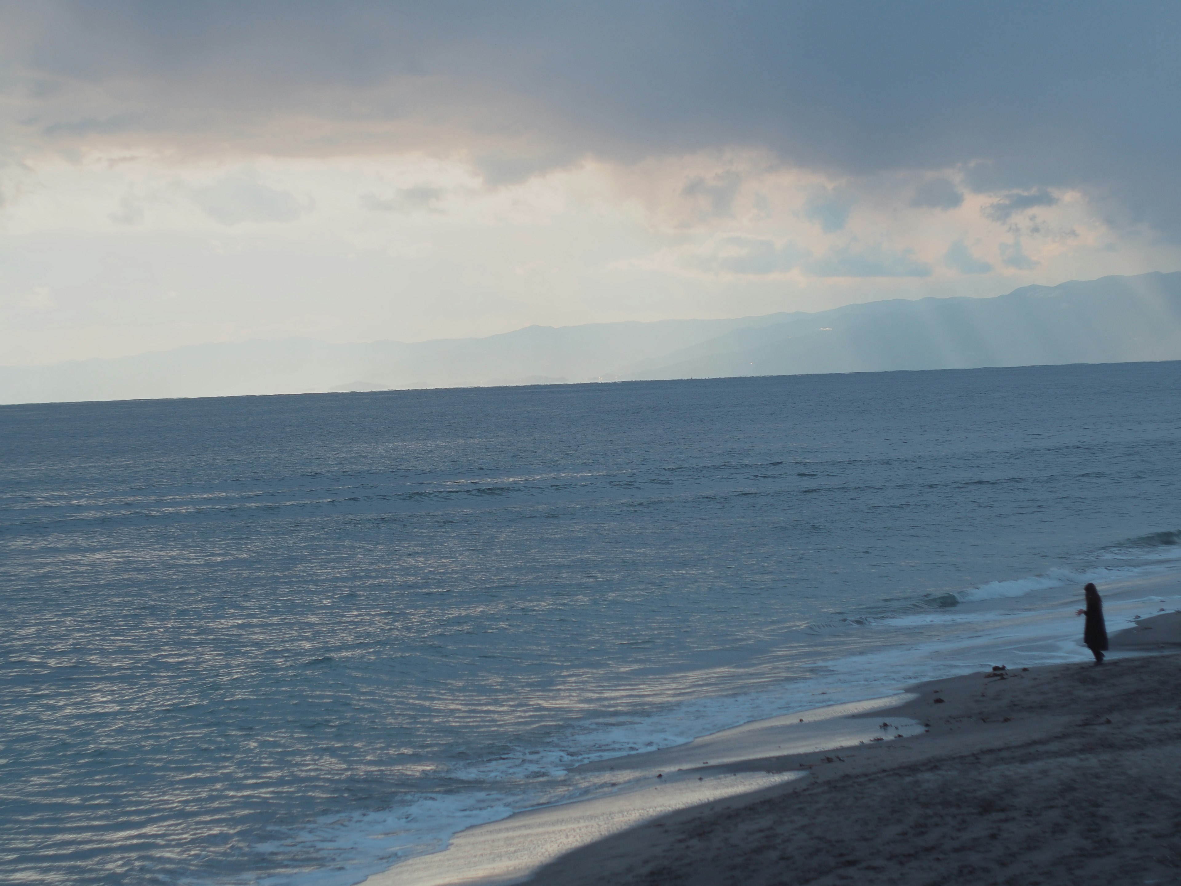 一個人站在海岸上，海浪和多雲的天空