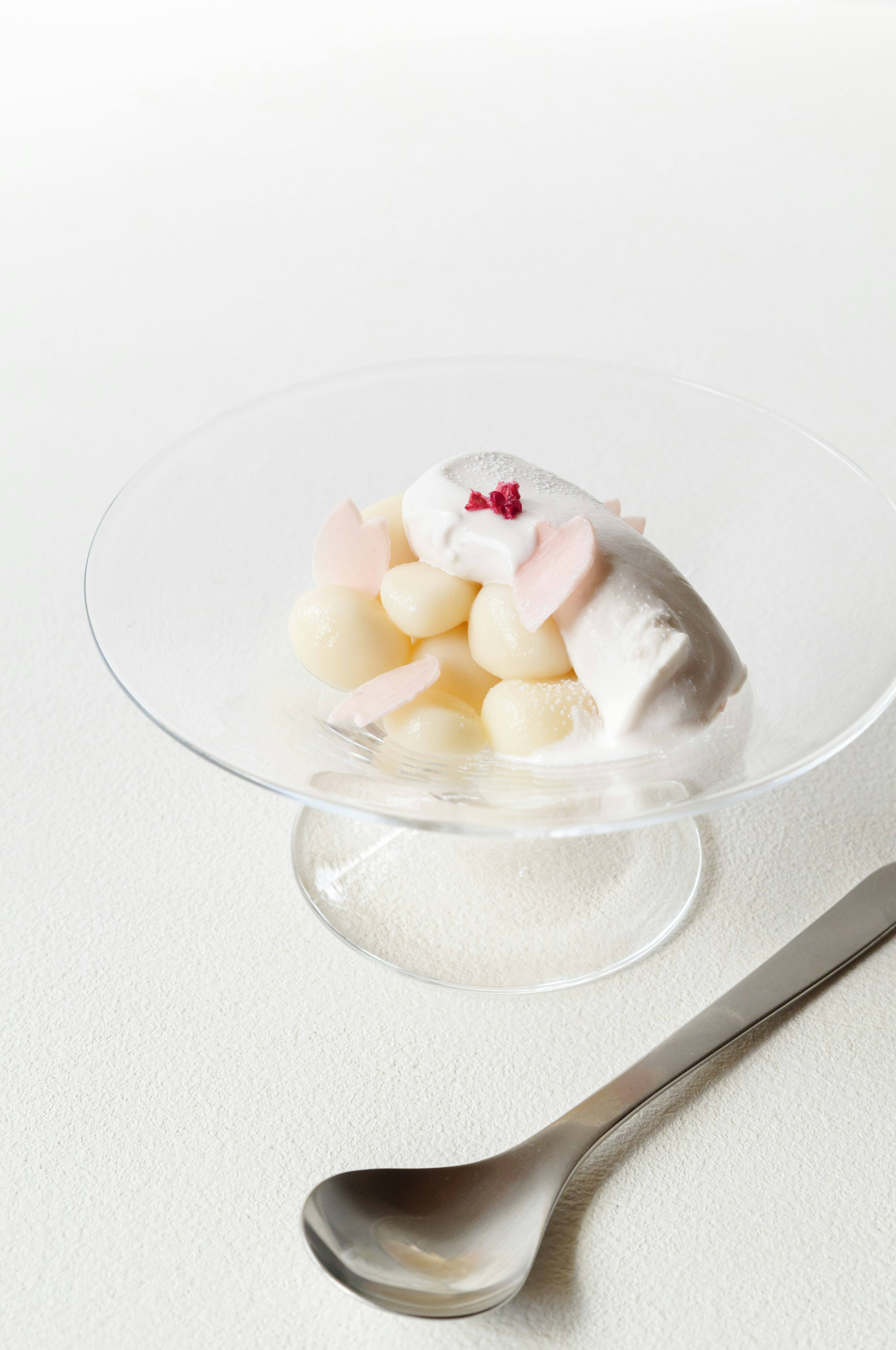 Un dessert blanc avec des garnitures roses servi sur une assiette transparente