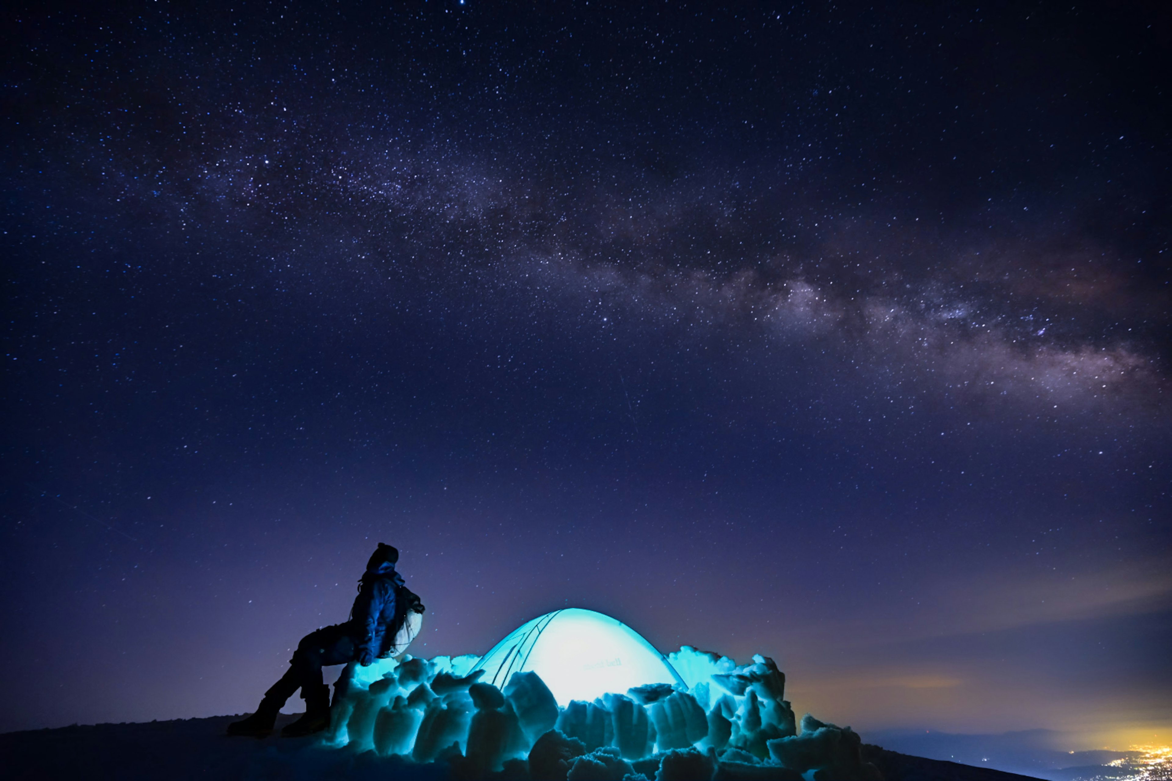 星空下坐在发光蓝色圆顶帐篷旁边的人