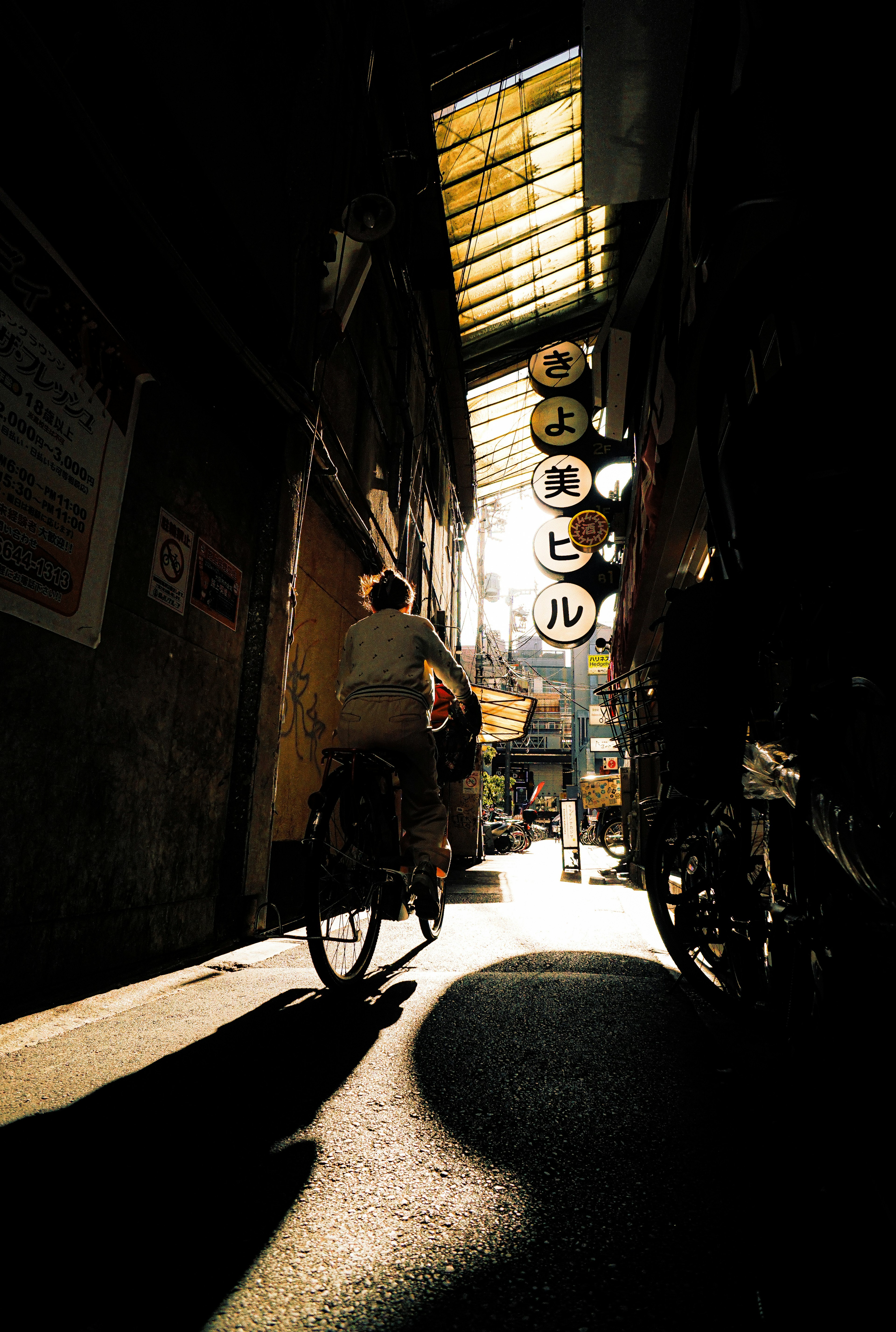 A person riding a bicycle through a narrow alley with sunlight streaming in