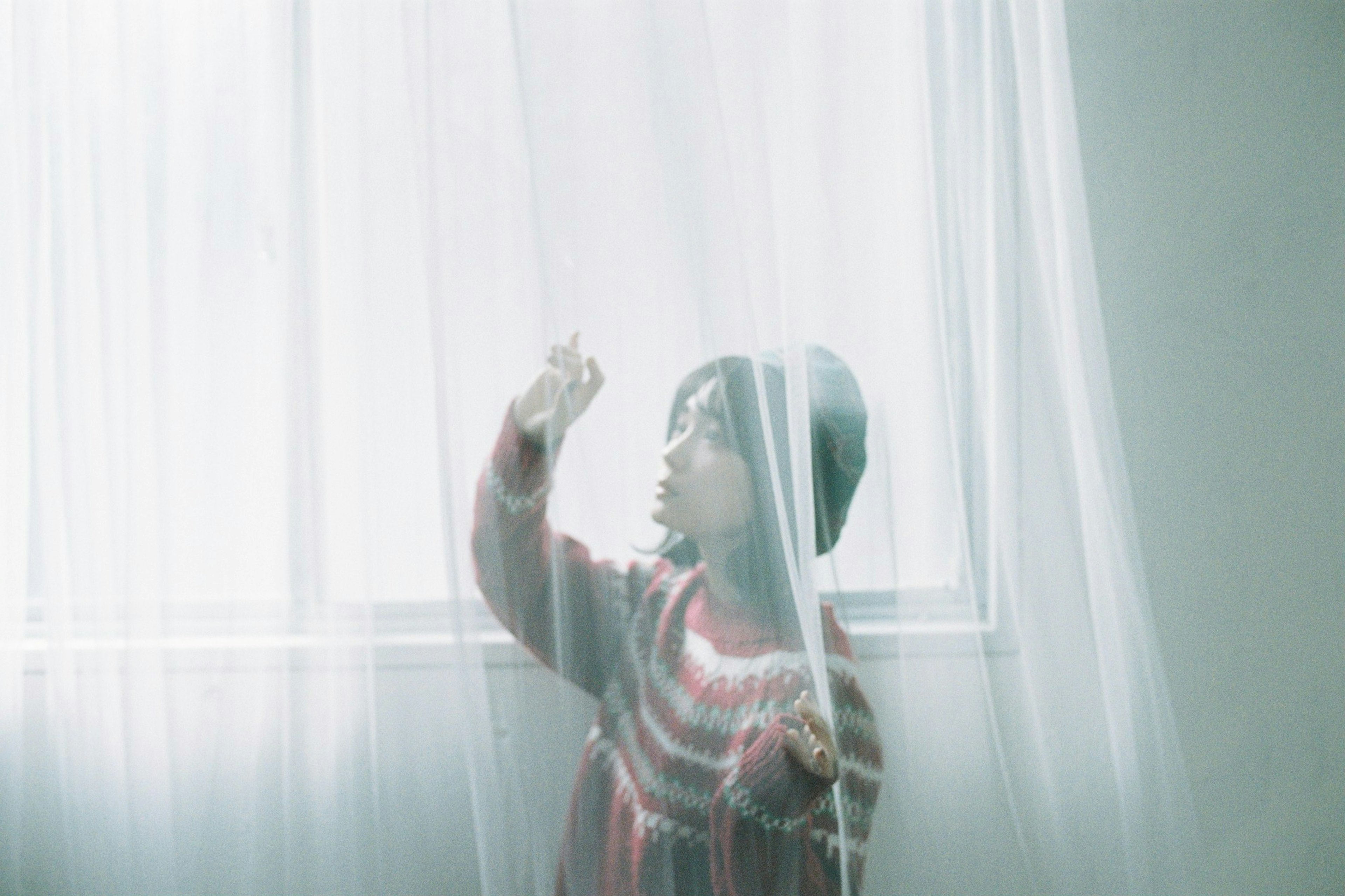 Child playing with white curtains near a window