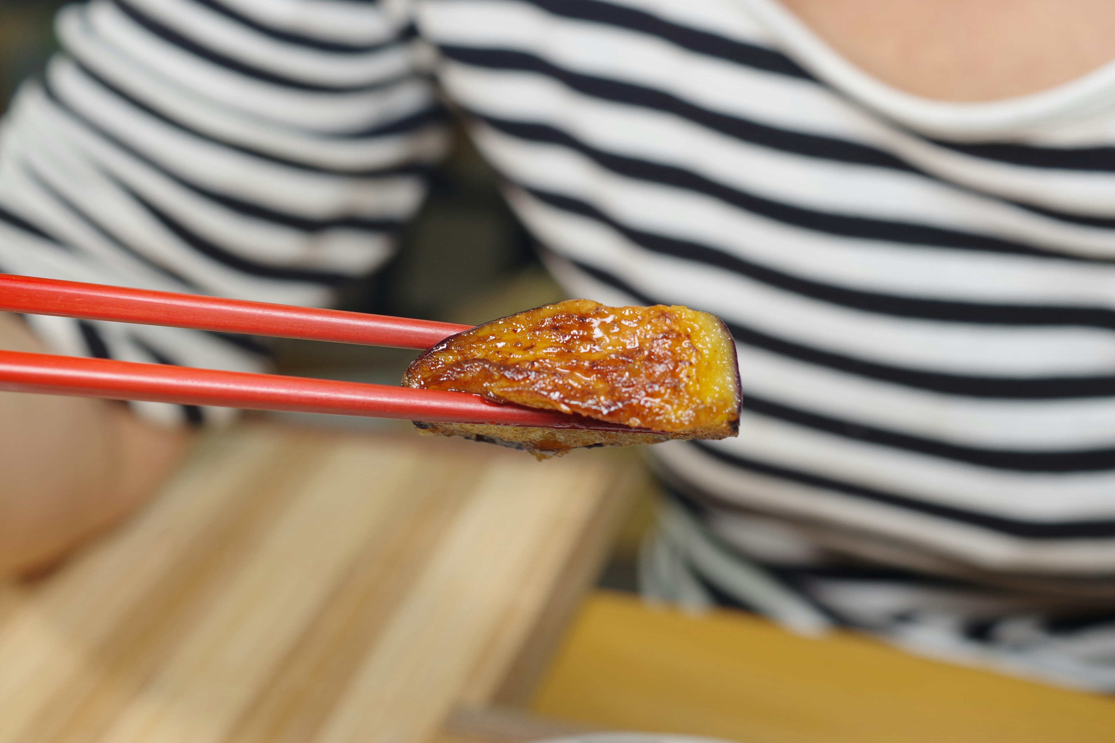 Un pezzo di pesce grigliato tenuto con le bacchette rosse e una maglietta a righe