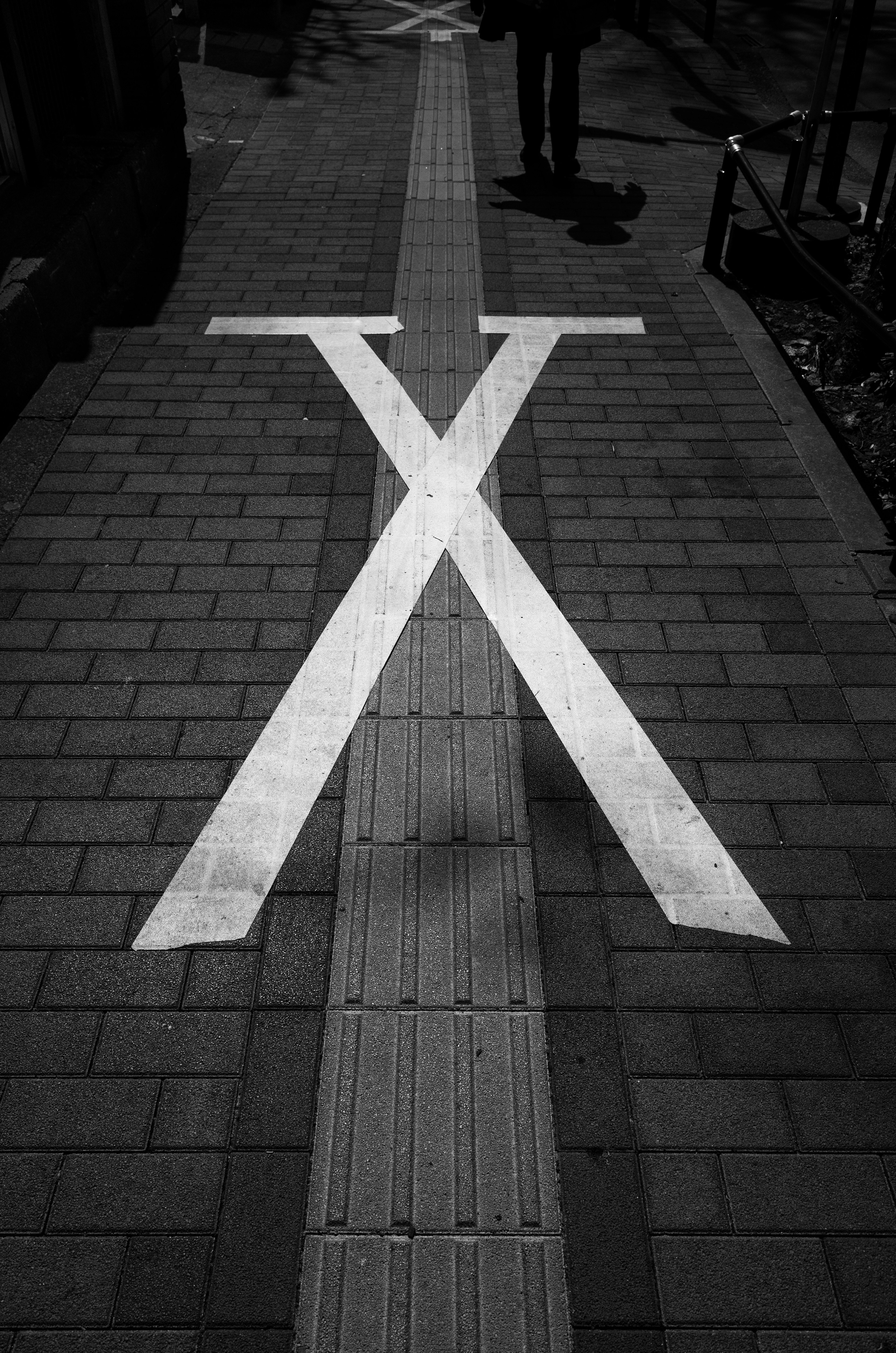 A black and white image of a sidewalk featuring a large white X mark