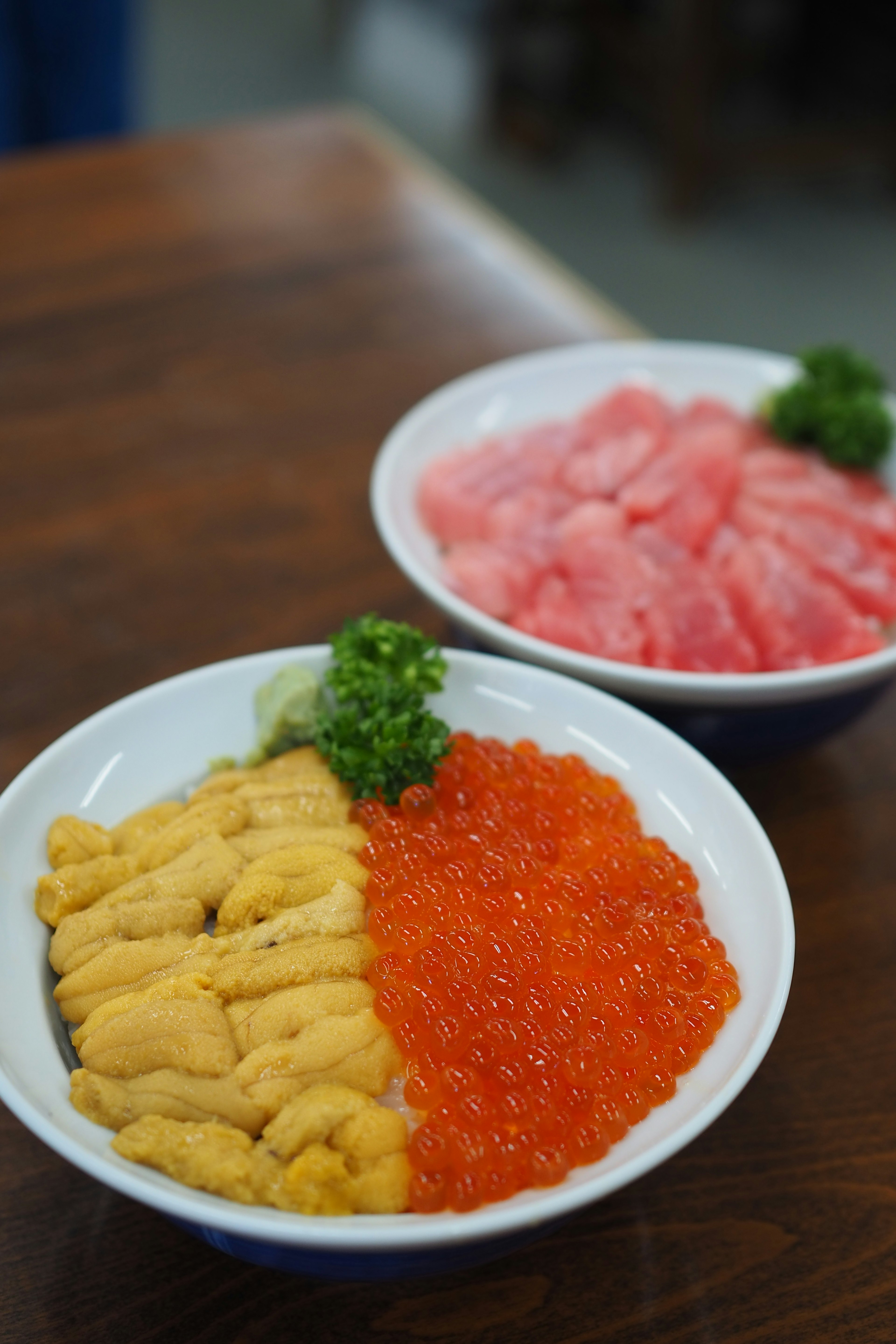 Two bowls of seafood featuring uni and ikura in one bowl and sashimi tuna in the other