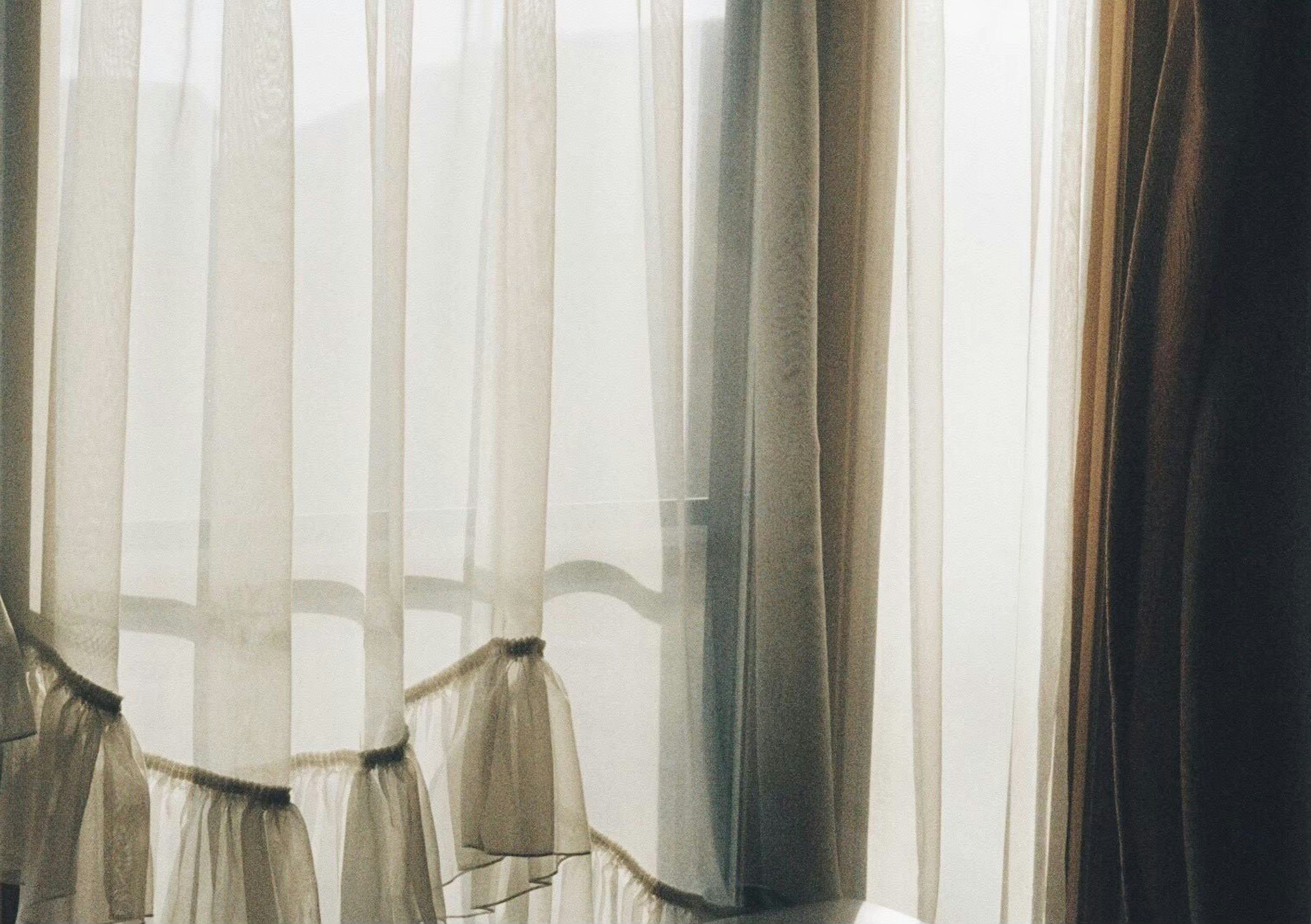 Close-up shot of sheer white curtains allowing soft light and warm-colored curtains