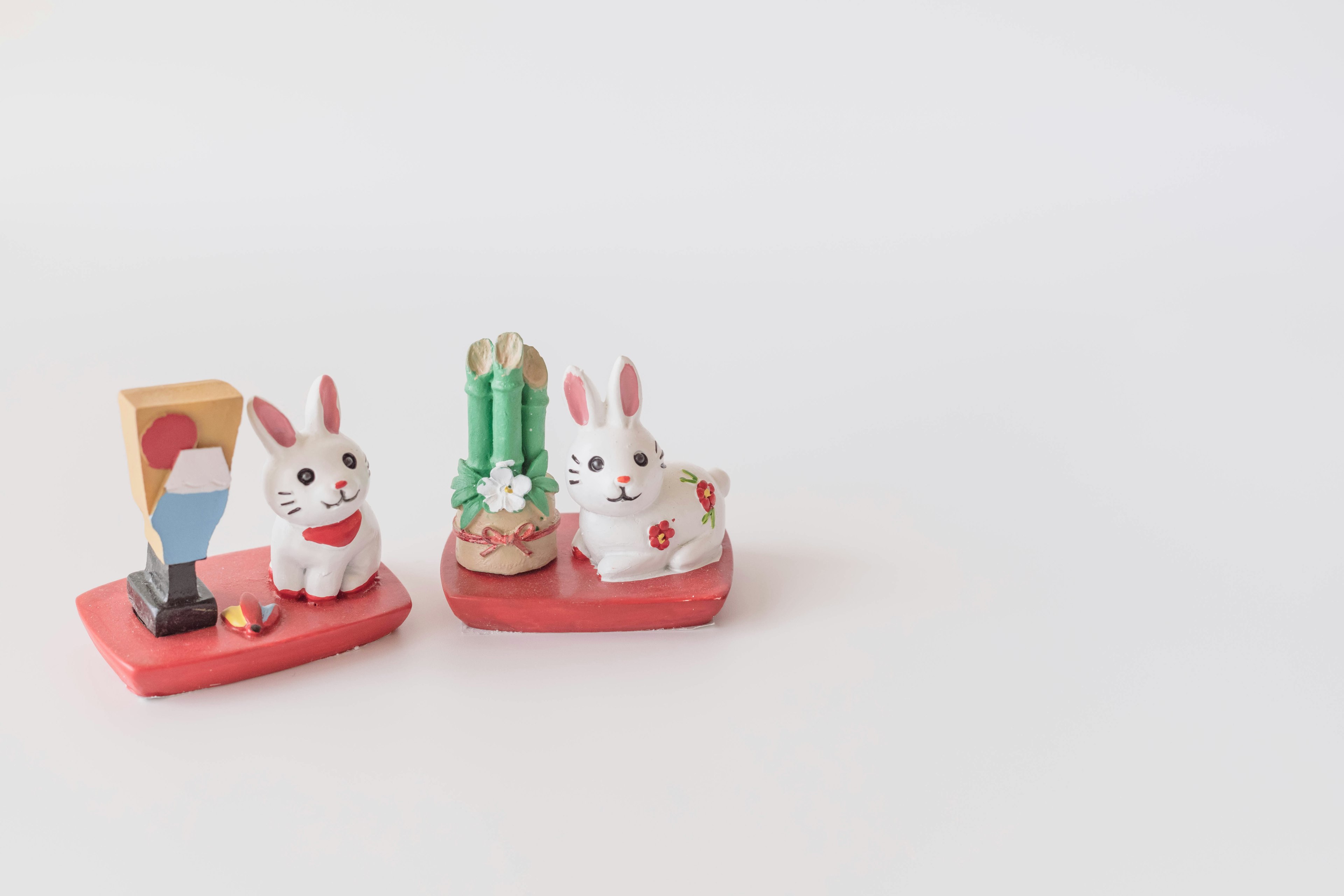 Two ceramic rabbits on a red base with a colorful mountain decoration and green bamboo