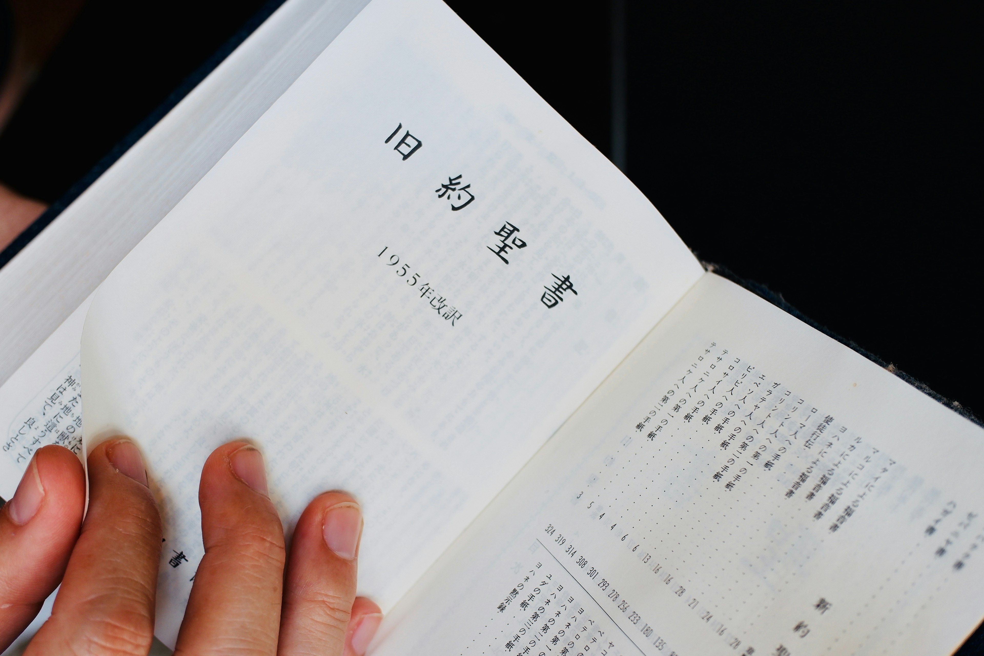 A close-up of a hand holding a book open to a page with Japanese text and vintage print style