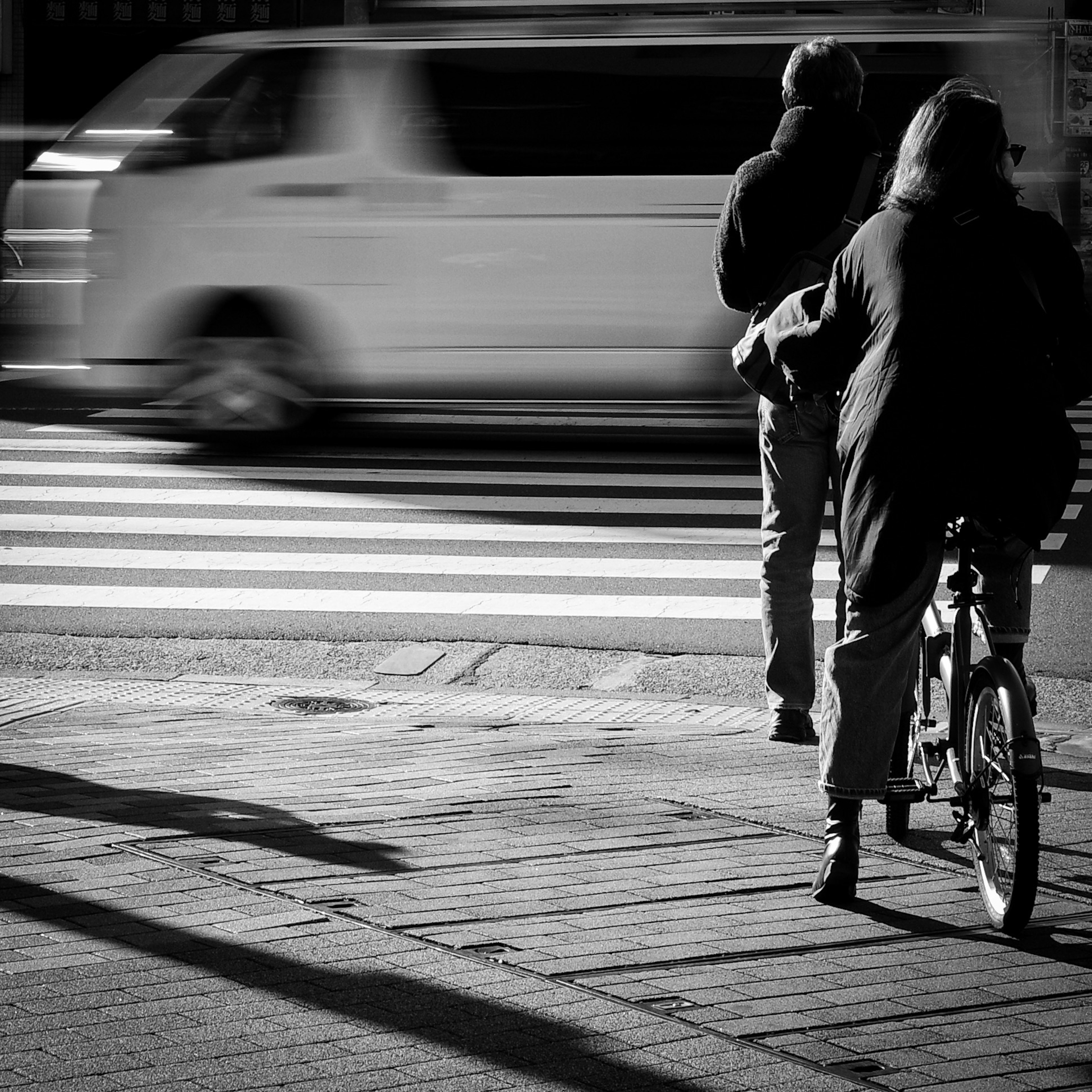 黑白場景中，一名女性騎自行車和一名行人在街角過馬路