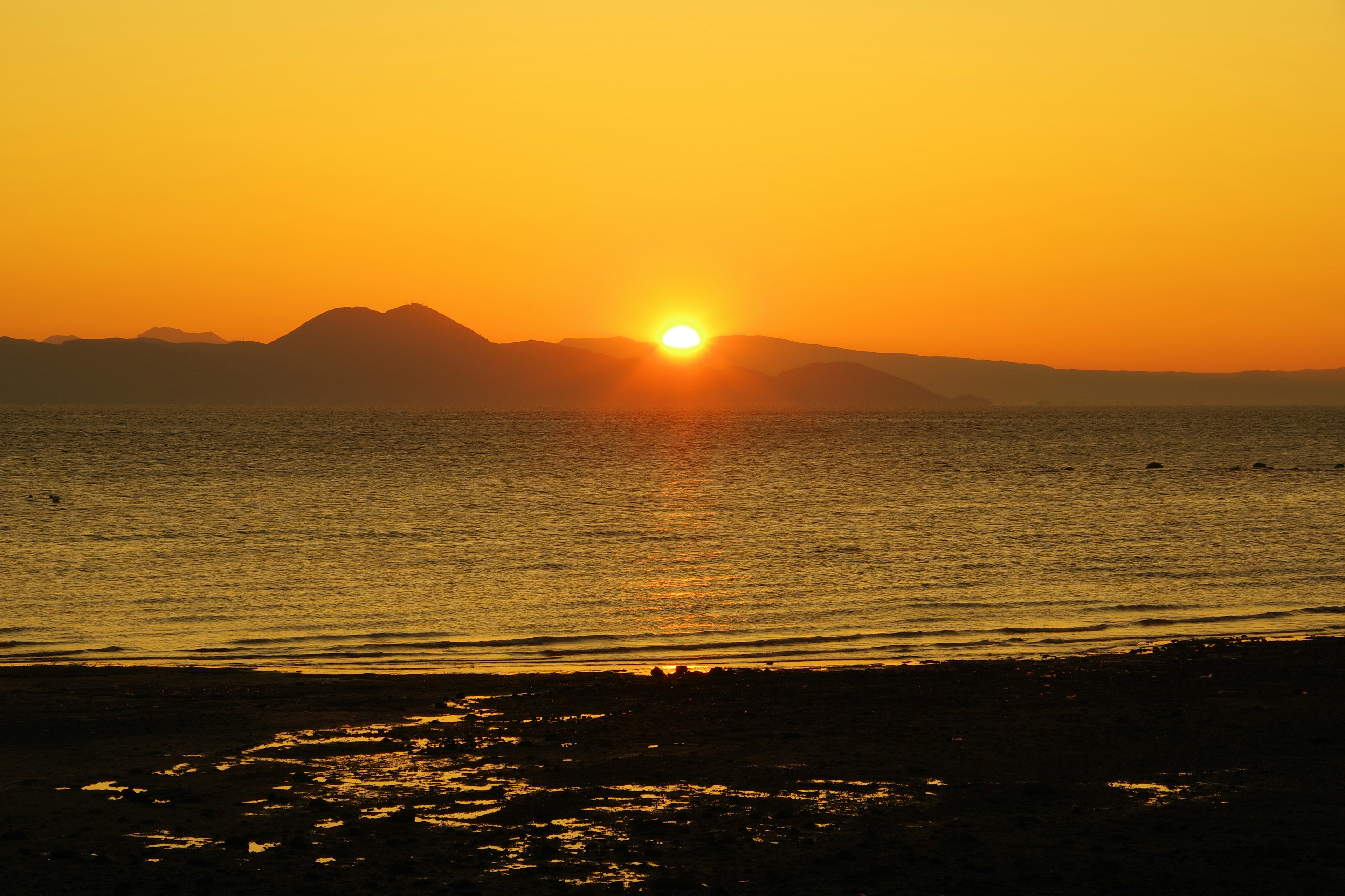 Wunderschöner Sonnenuntergang über dem Ozean mit Silhouetten von Bergen