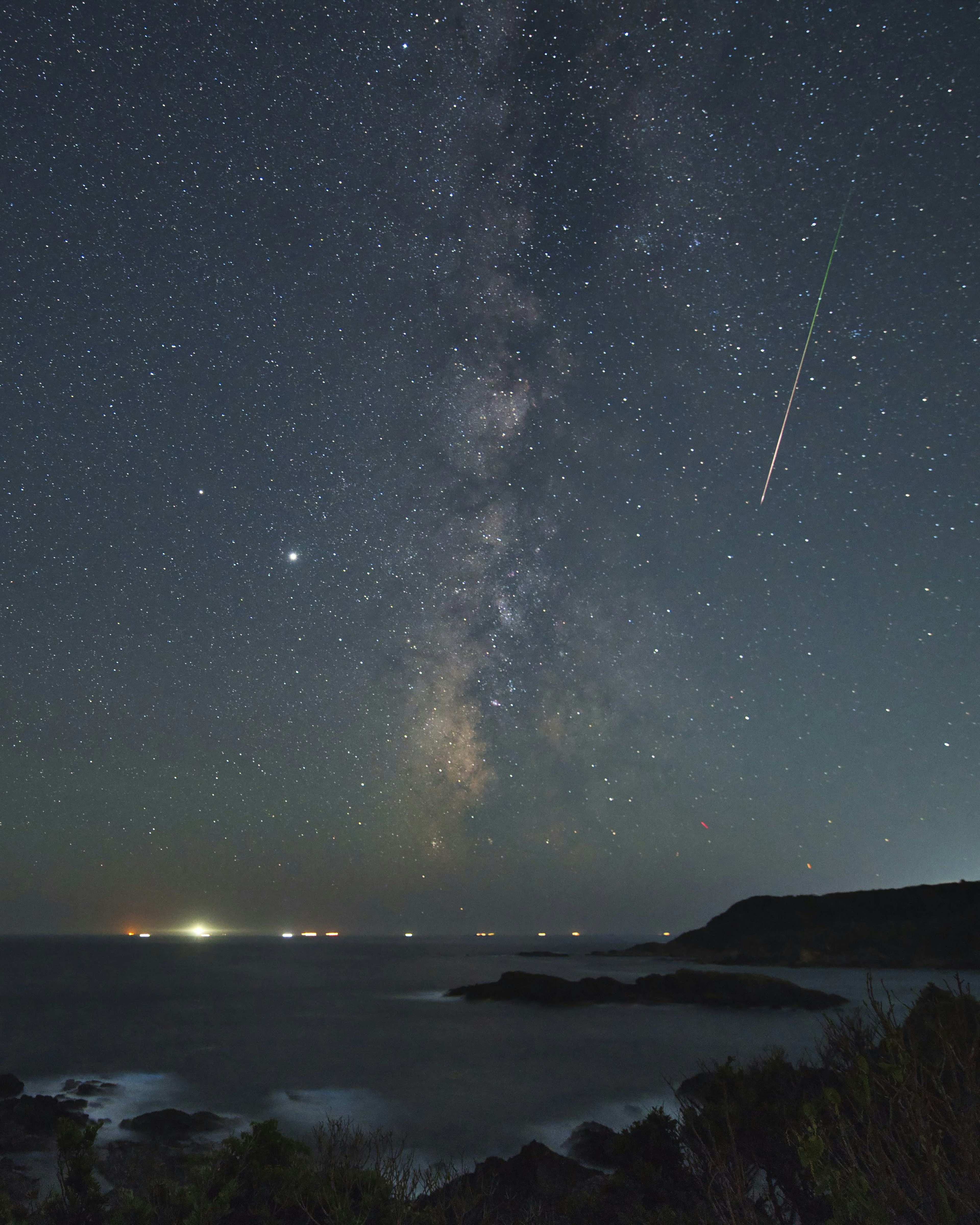 Coastal scene with a starry sky and the Milky Way A shooting star crosses the night sky