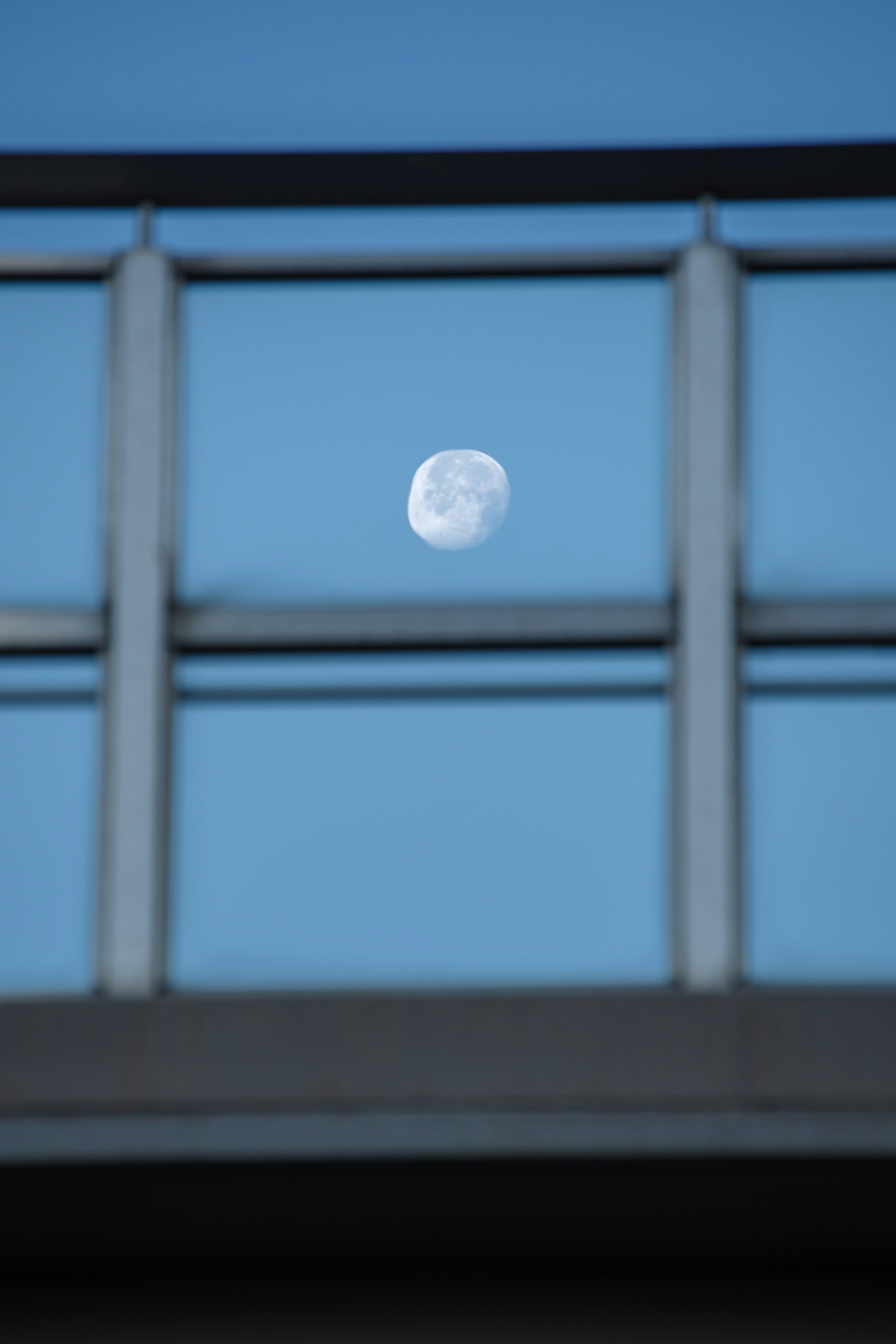 Moon visible through a window frame against a blue sky