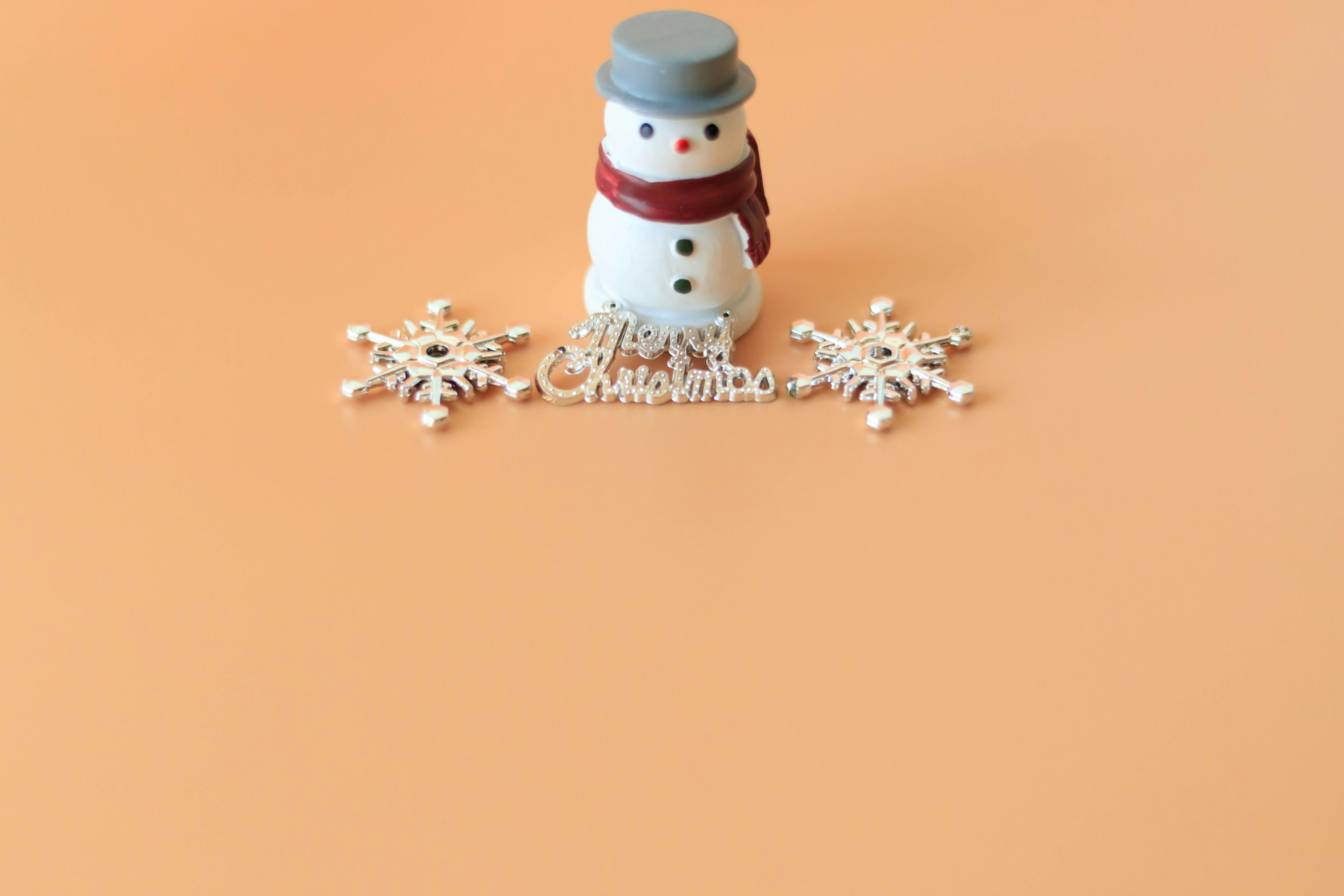 Un muñeco de nieve con un sombrero gris y una bufanda roja rodeado de copos de nieve sobre un fondo naranja